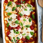 Baked Gnocchi in a white baking dish with marinara sauce, mozzarella and basil.