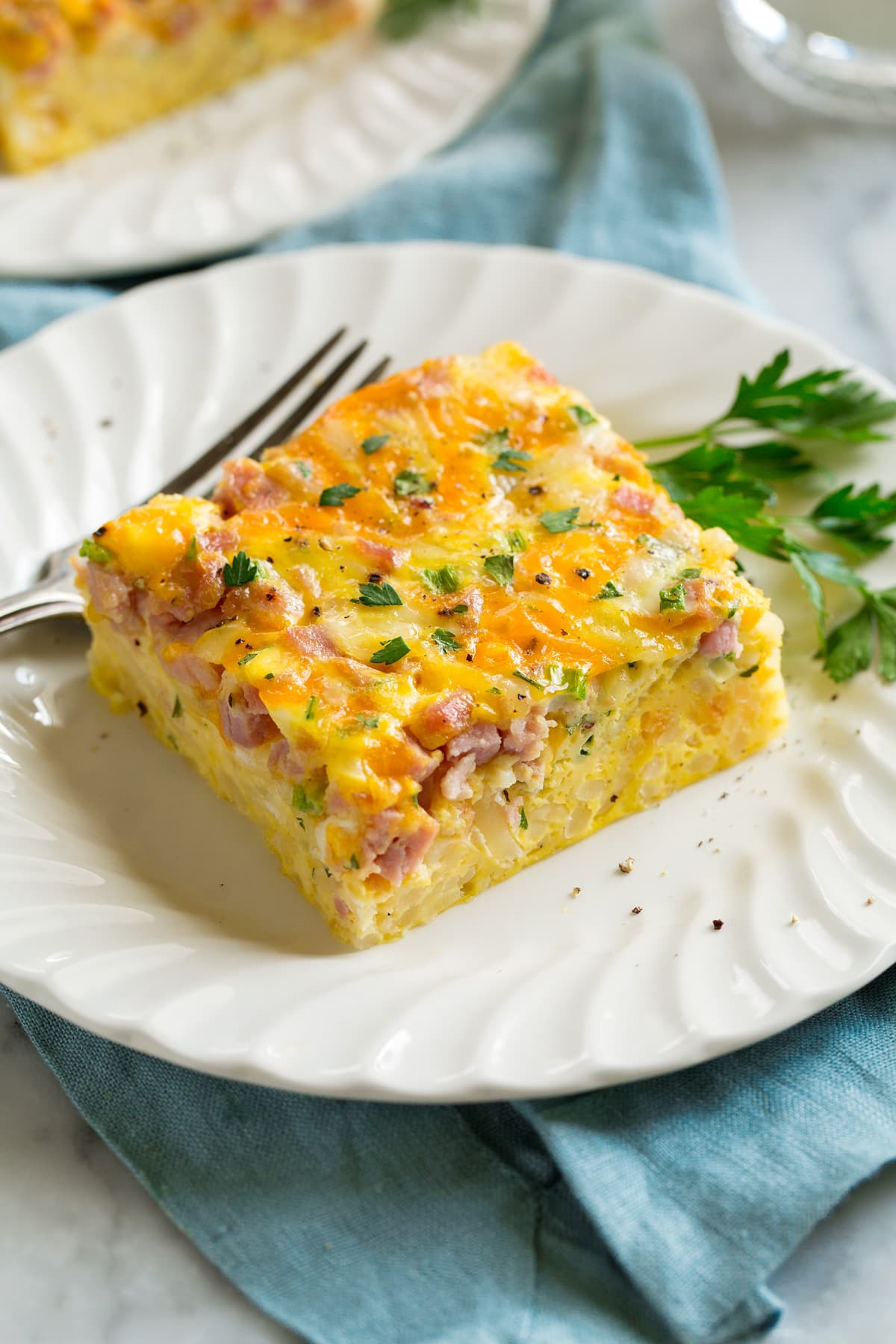 Breakfast Casserole Slice of breakfast casserole filled with eggs, hash browns, ham and cheese on a white serving plate.