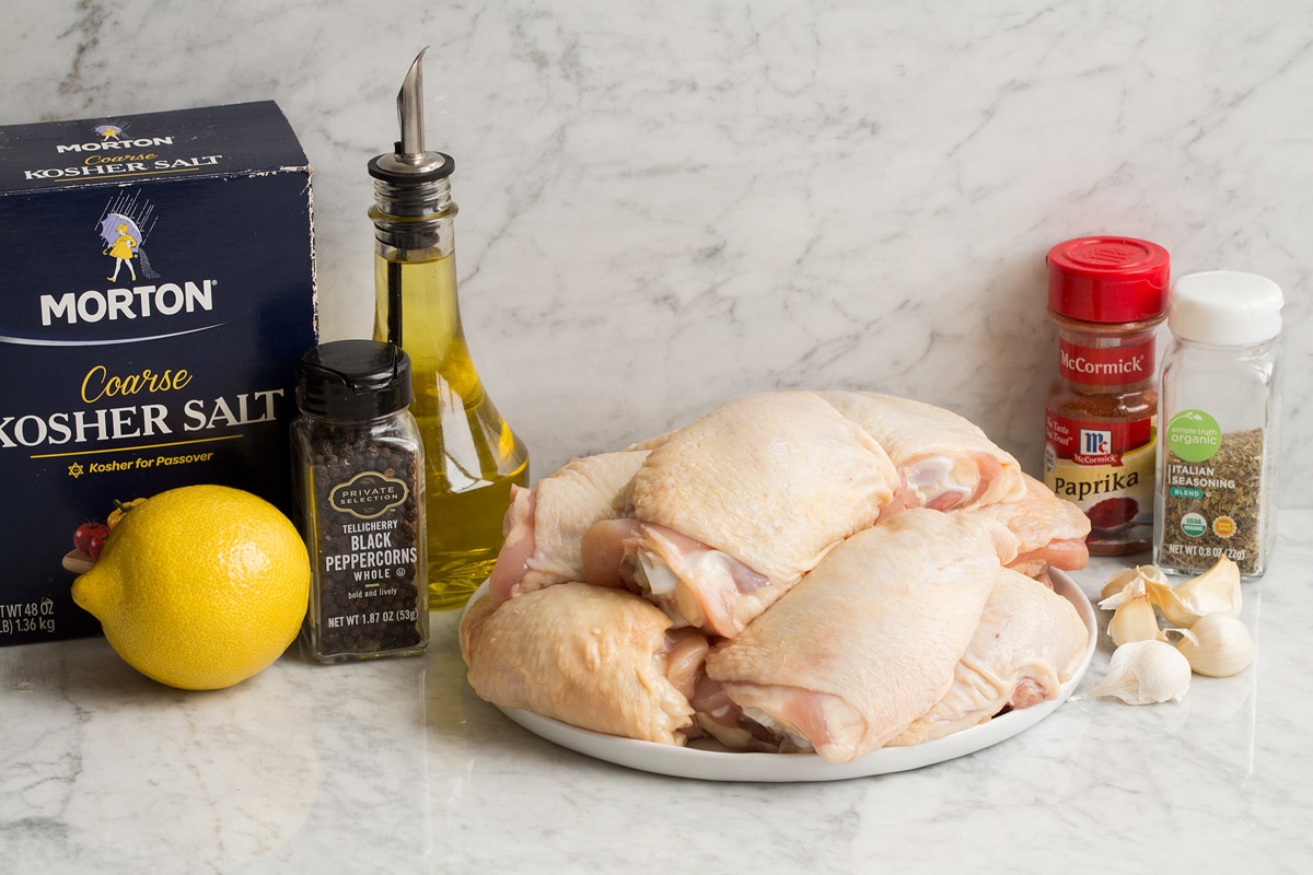 Baked Chicken Thighs Image of ingredients needed to make baked chicken thighs. Shows raw chicken thighs, salt and pepper, olive oil, lemon, paprika, Italian seasoning and garlic.