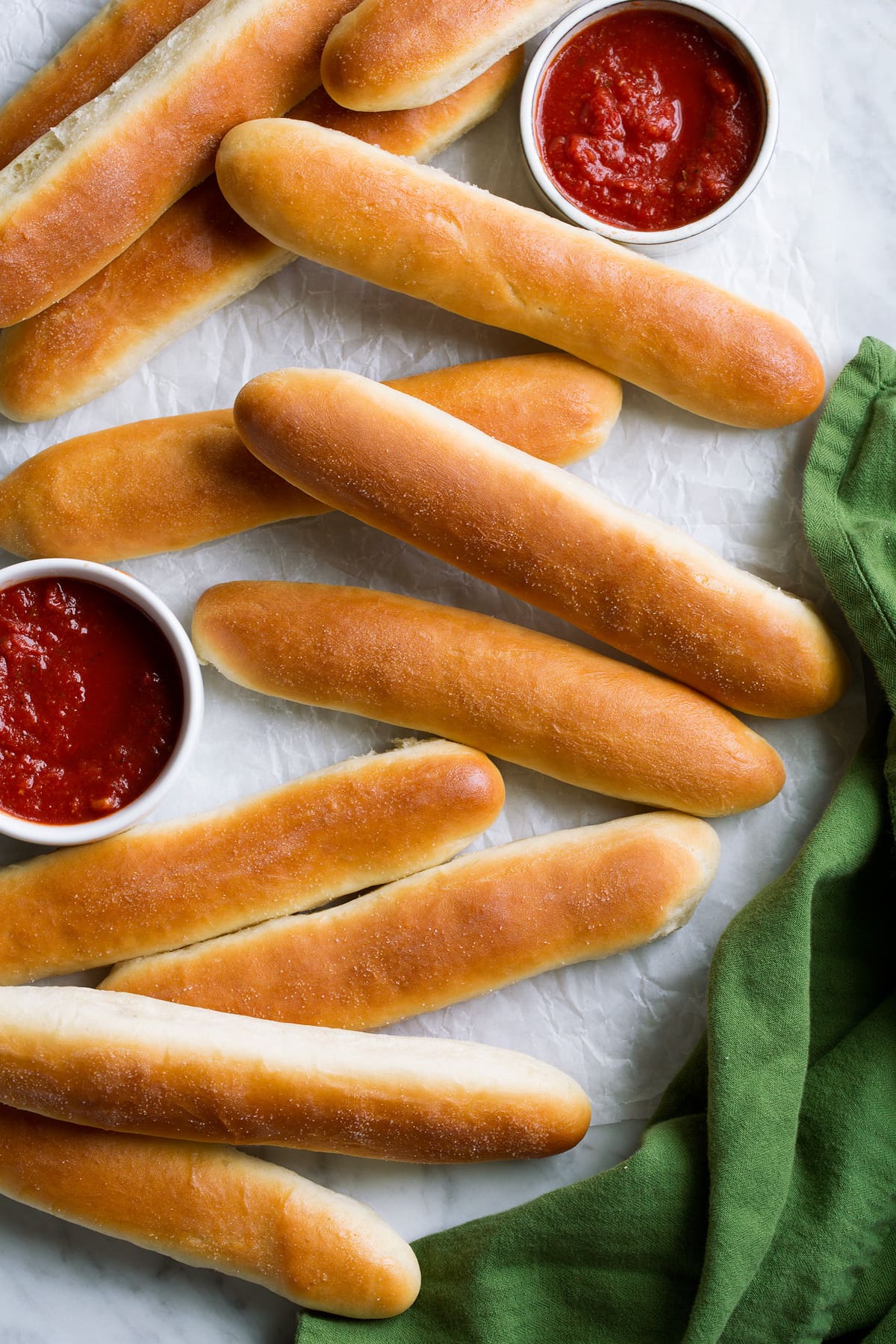 Breadsticks Recipe (Olive Garden Copycat) Breadsticks spread out onto parchment with sides of marinara sauce.