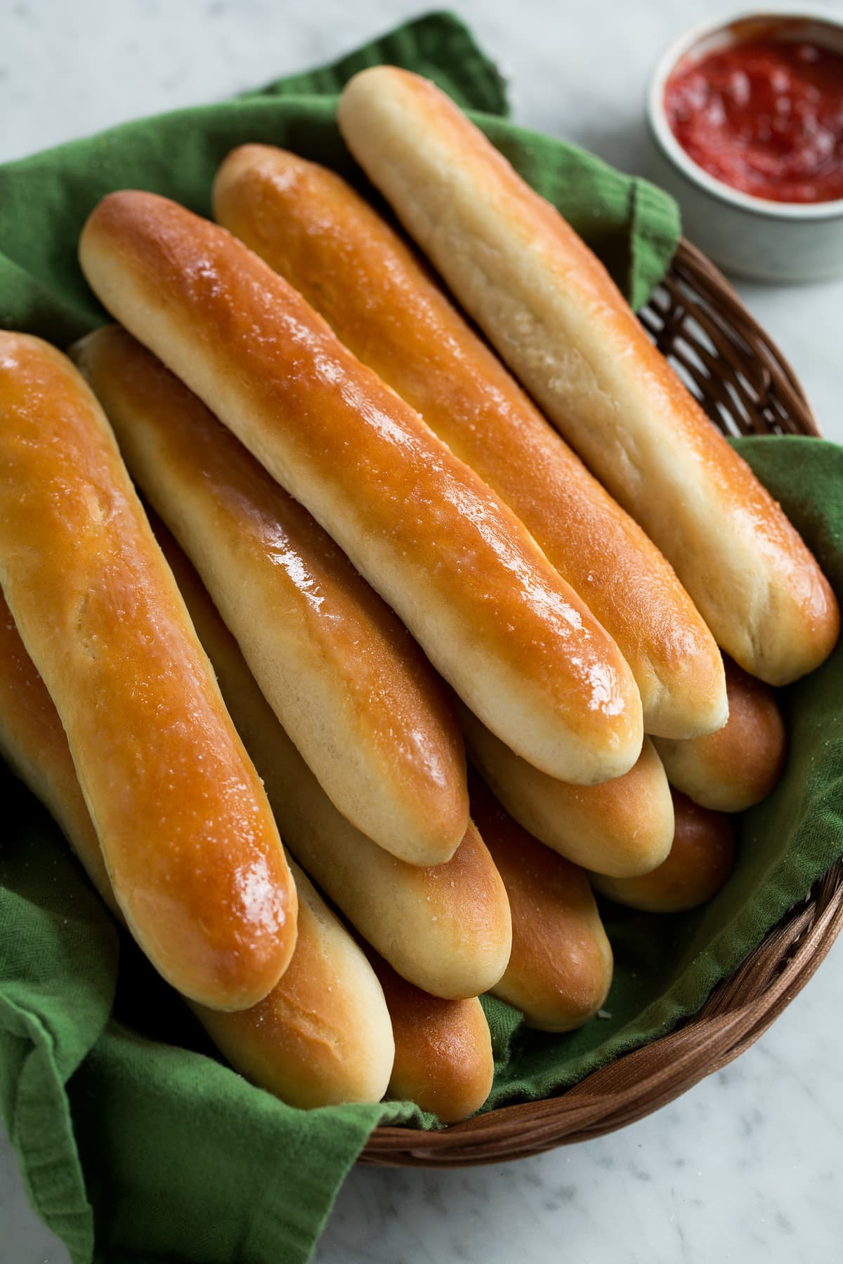 Breadsticks Recipe (Olive Garden Copycat) Breadsticks stacked in a wicker basket lined with a green kitchen cloth.
