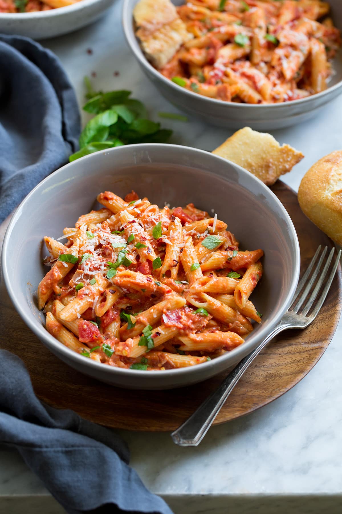 Vodka Sauce Two servings of penne alla vodka in grey serving bowls set over wooden plates.