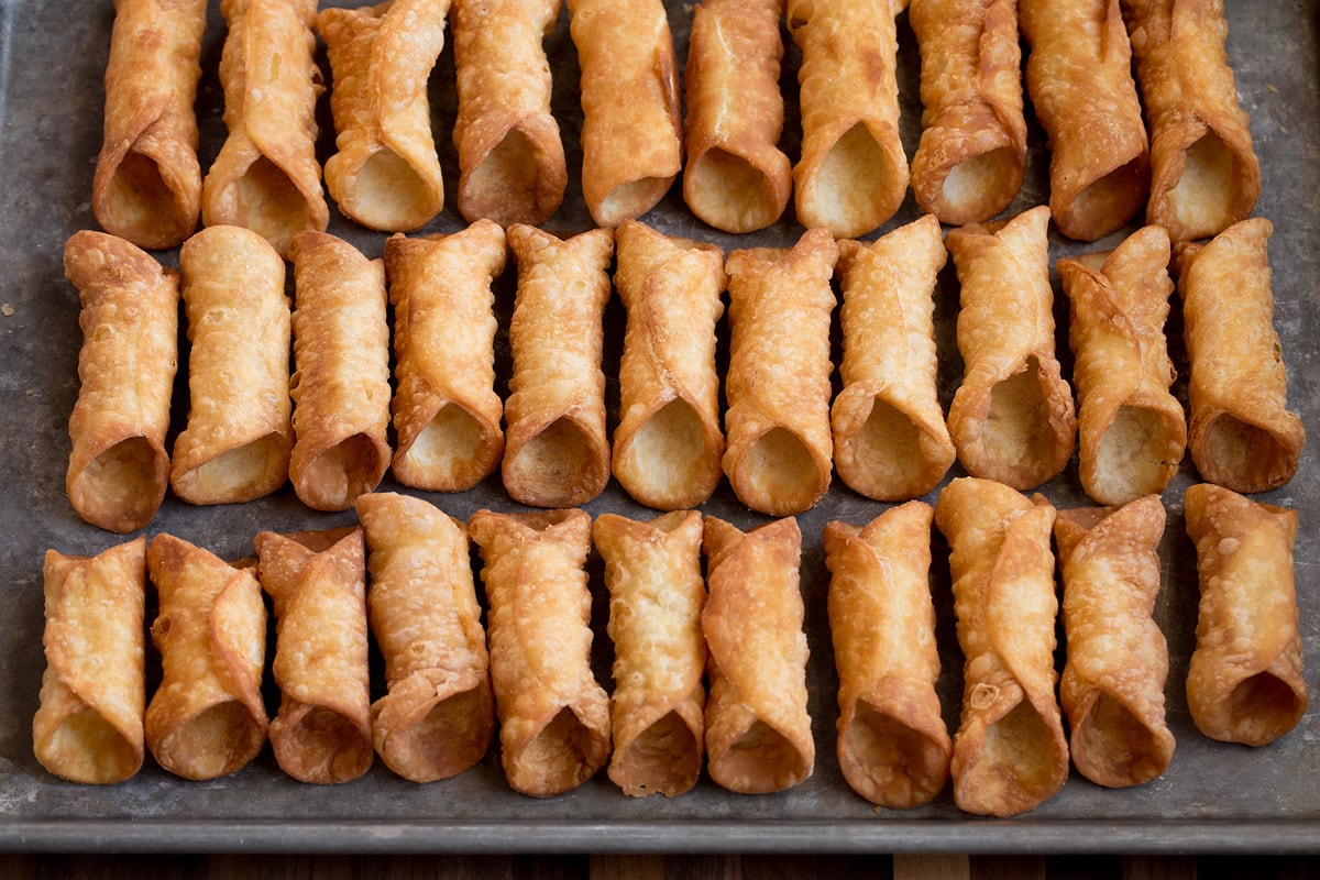 Cannoli Shells Homemade fried cannoli shells on a baking sheet shown before filling.