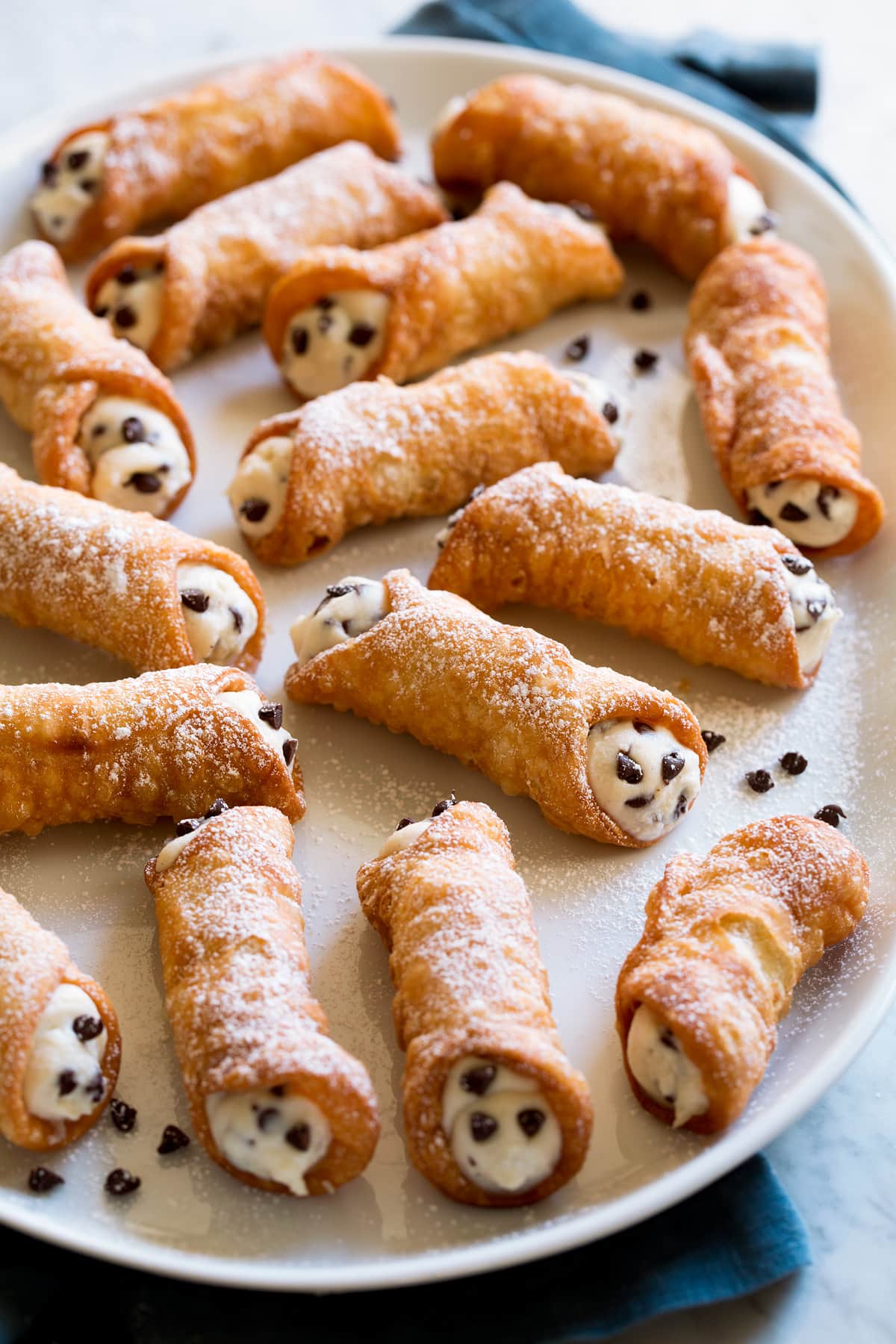 Cannoli Recipe Cannoli with ricotta and chocolate chip filling on a white serving platter.