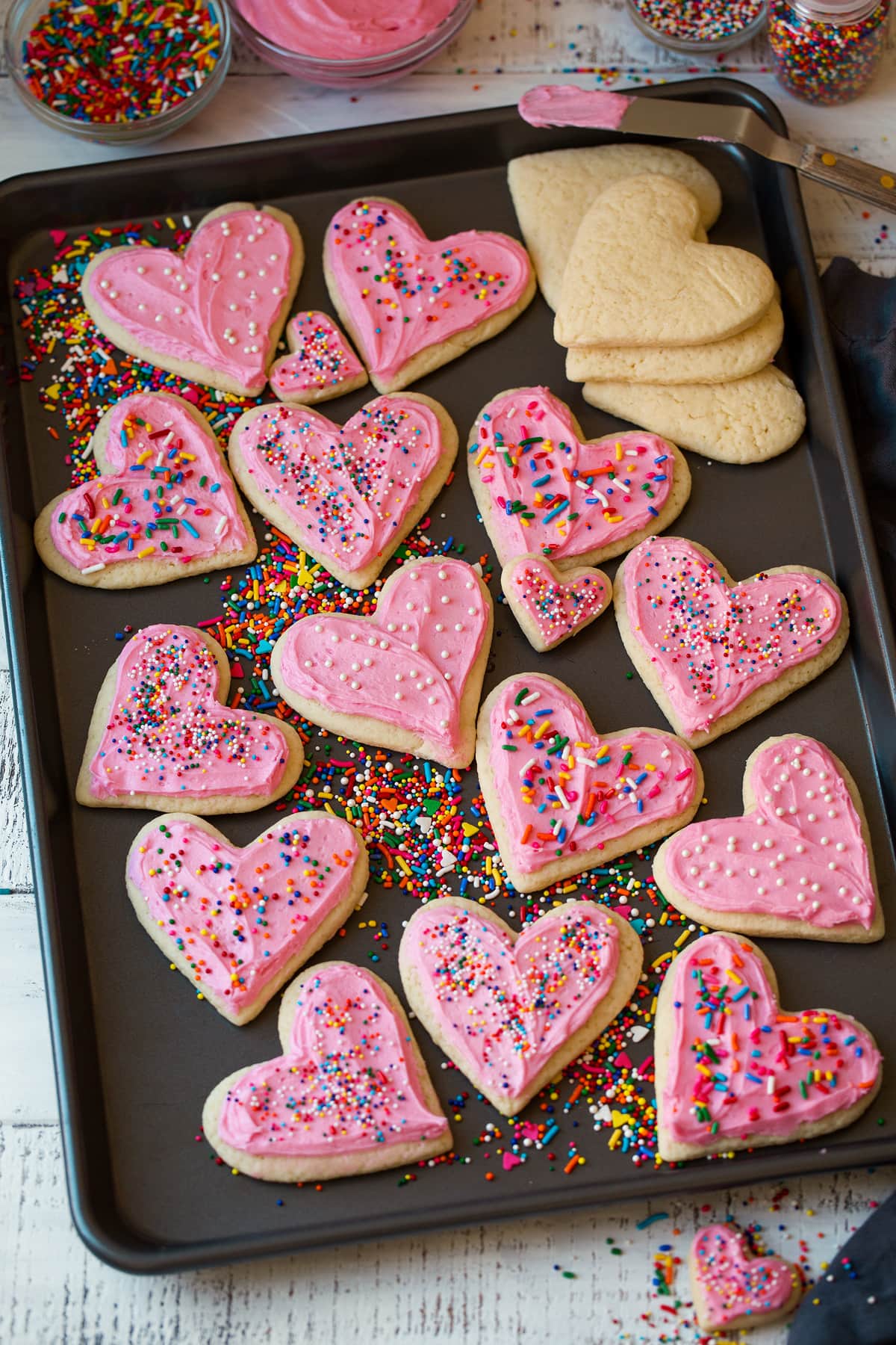 Soft Frosted Sugar Cookies Cutout sugar cookies in heart shapes on a baking sheet shown frosted with sprinkles.