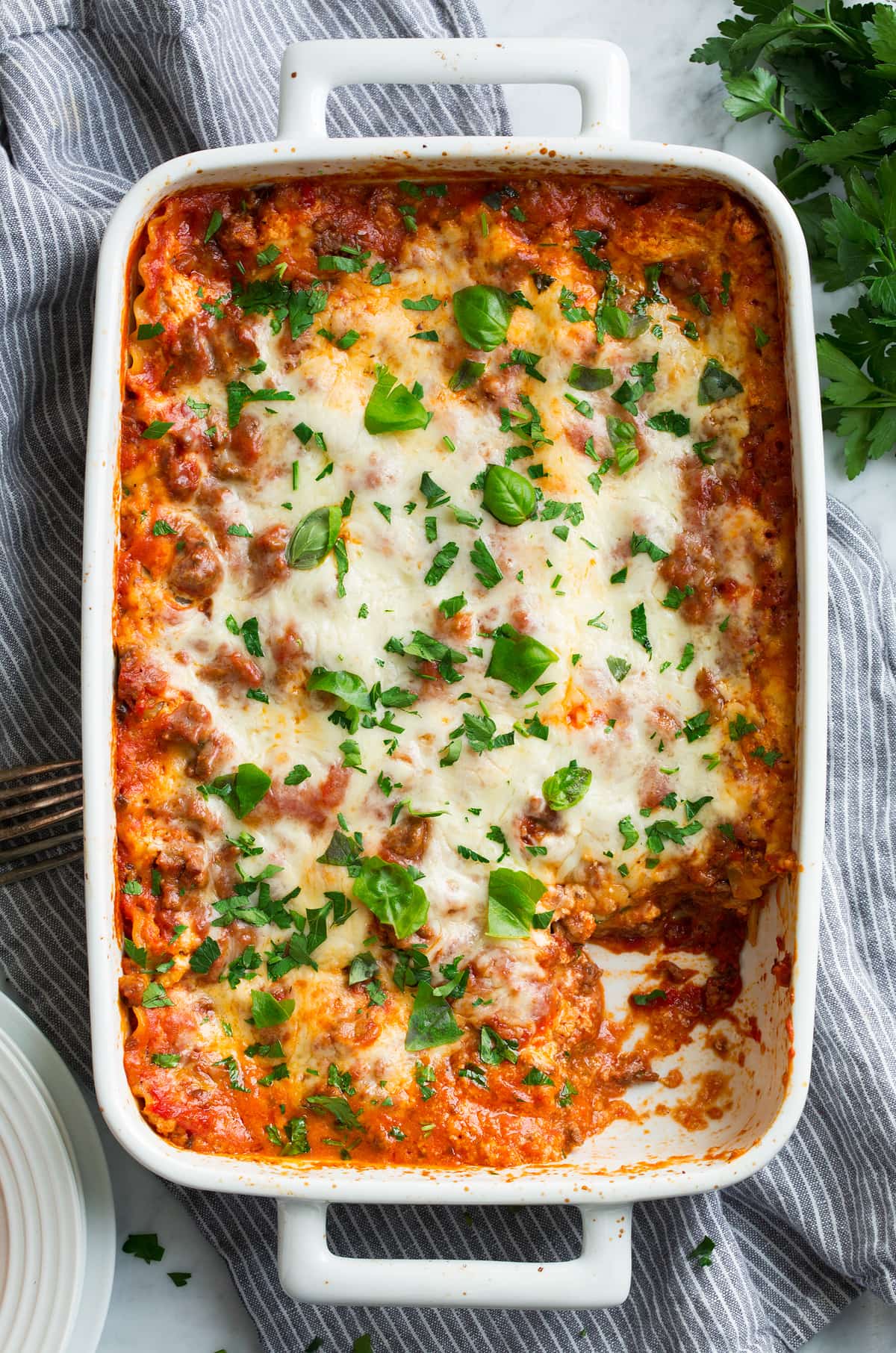 Easy Lasagna Recipe Easy lasagna shown overhead in a white casserole dish with one portion cut out.