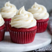 Cream cheese frosting shown piped over red velvet cupcakes.