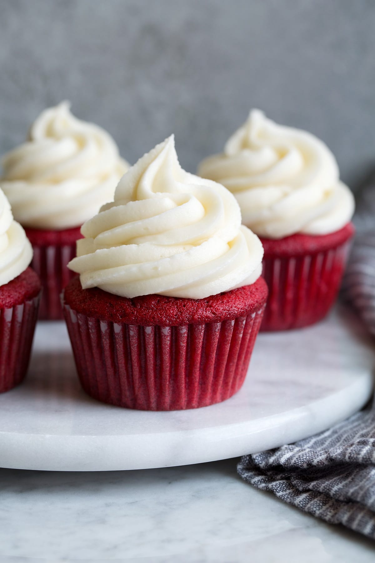 Cream Cheese Frosting Cream cheese frosting shown atop four red velvet cupcakes on a marble platter.