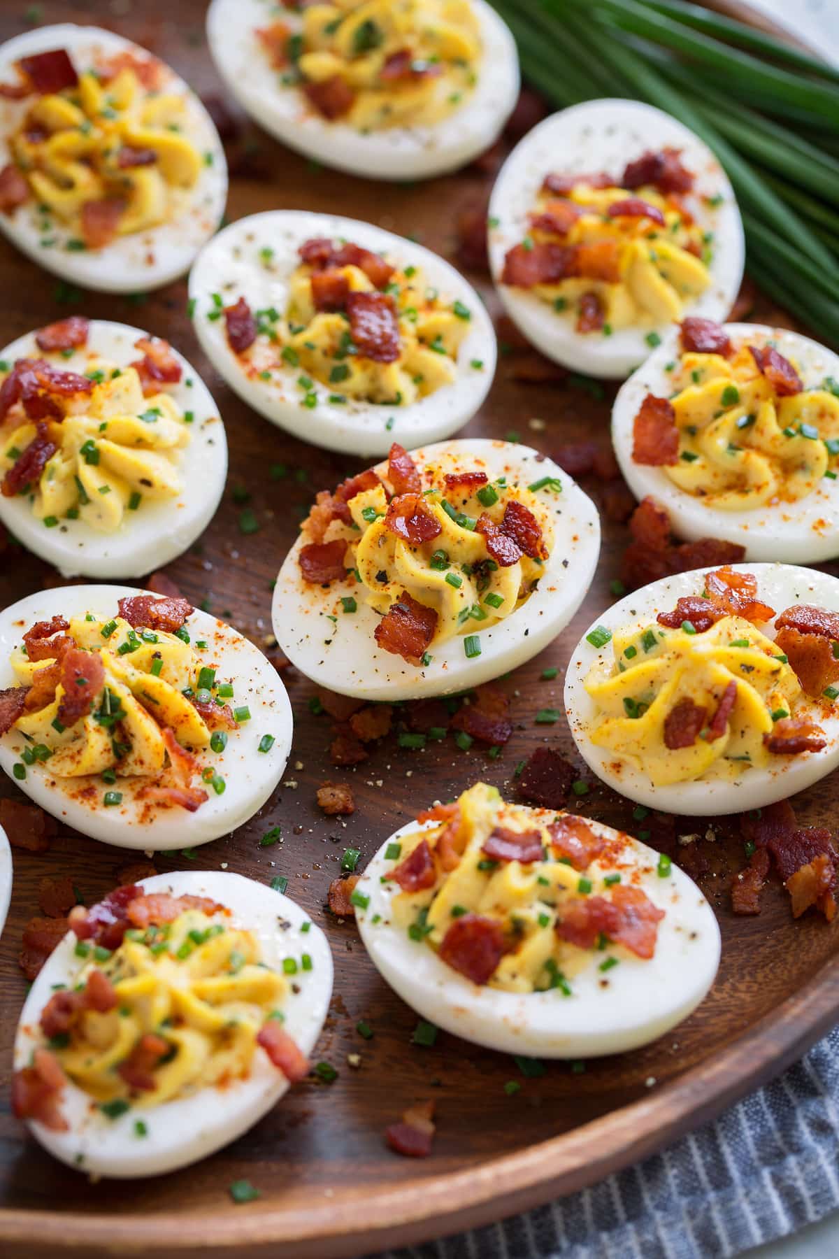 Deviled Eggs Wooden plate filled with deviled eggs. Eggs filled with a creamy mayonnaise and egg yolk filling and are garnished with chives and bacon.