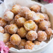 Homemade donuts in a serving bowl. Two are bitten into to show texture of interior.