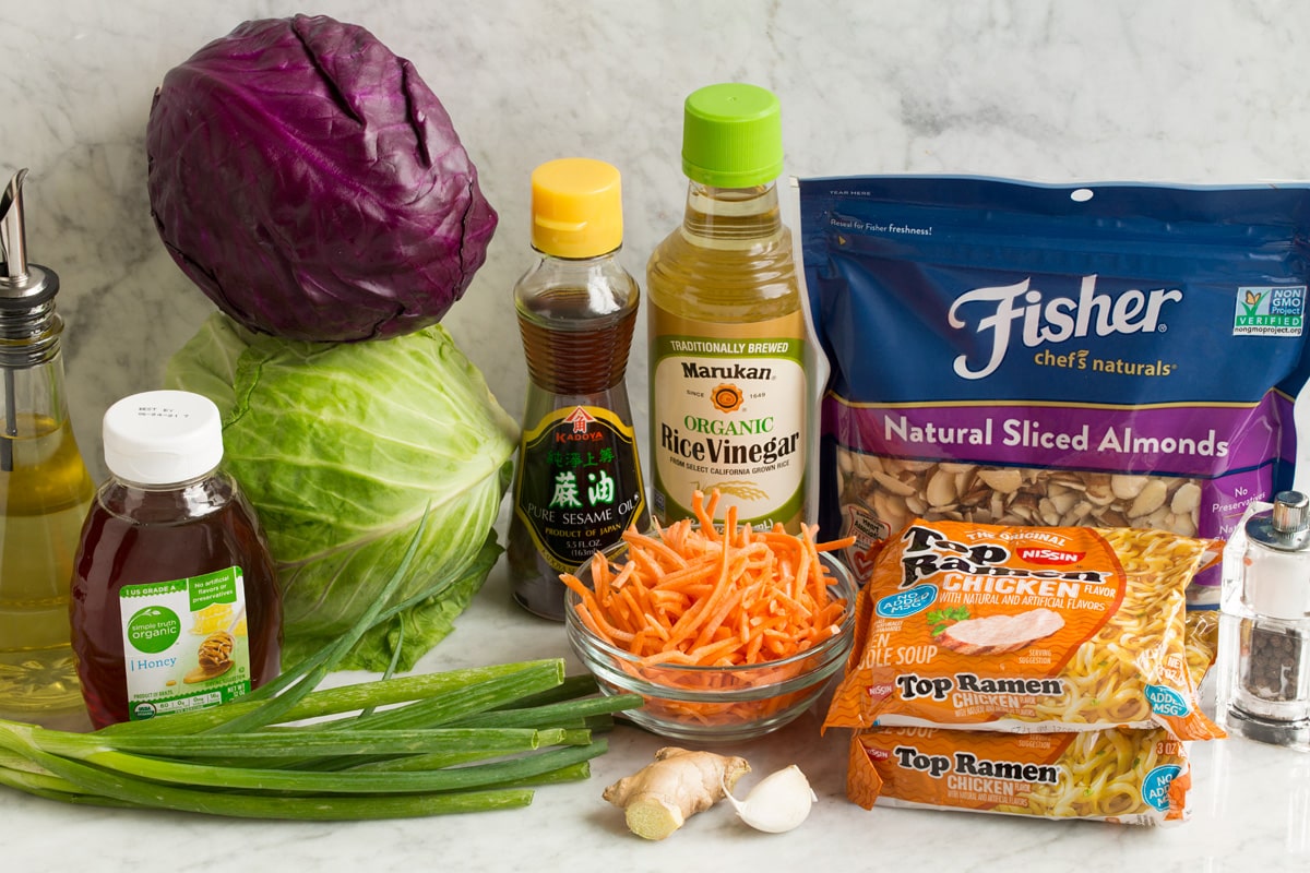Asian Ramen Noodle Salad Ingredients used to make Asian ramen noodle salad shown in this image. Includes red and green cabbage, carrots, almonds, dry ramen noodles, honey, rice vinegar, sesame oil, garlic, ginger and oil.