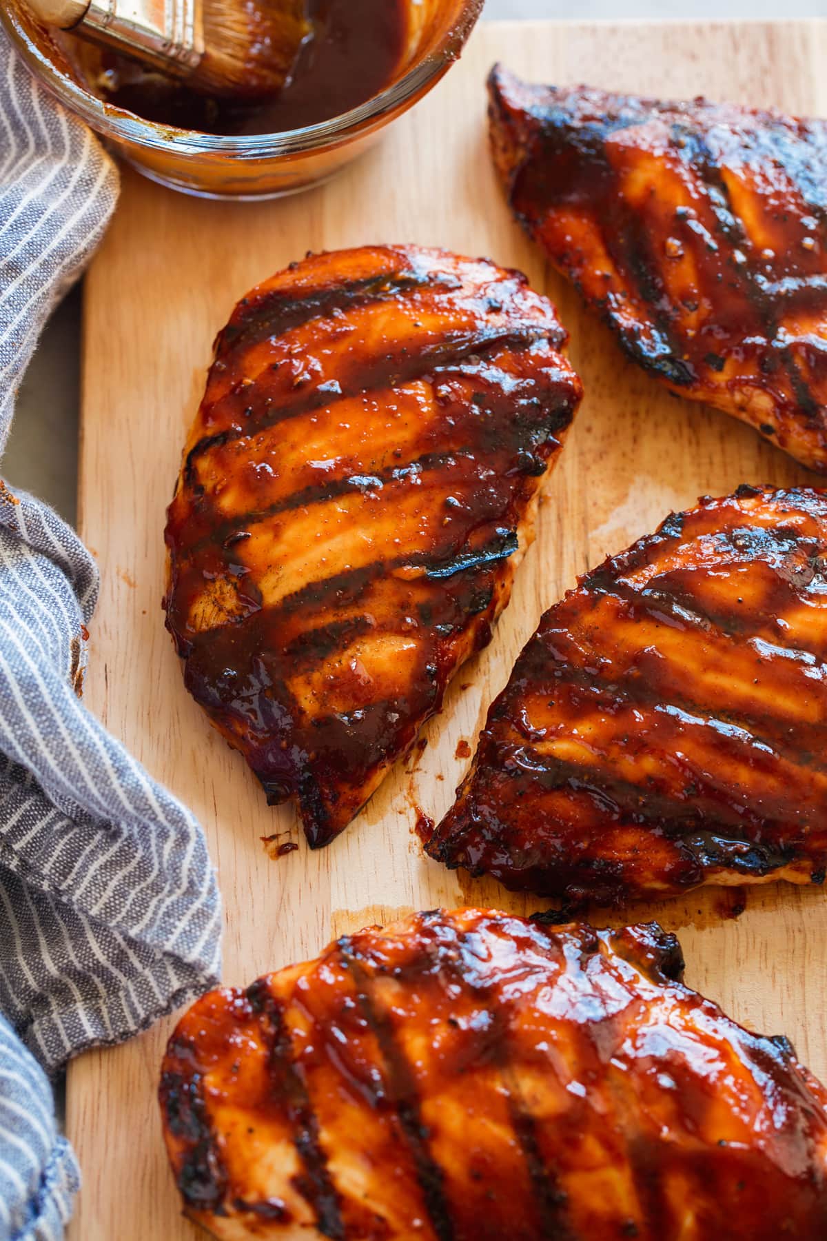Homemade BBQ Sauce Grilled chicken breasts covered in bbq sauce on a wooden cutting board.