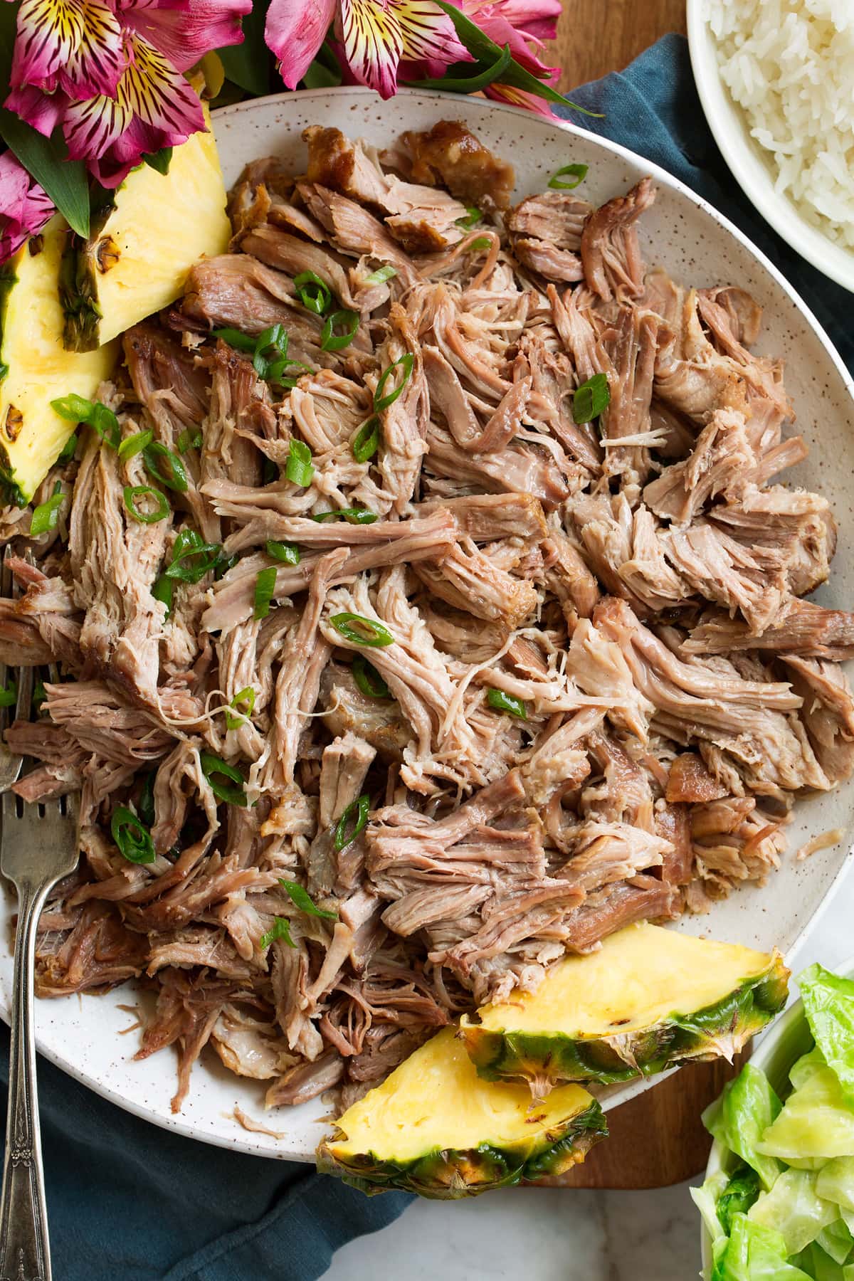 Kalua Pork Overhead image of shredded Kalua pork in a white serving bowl with pineapple. It is garnished with sliced green onions.