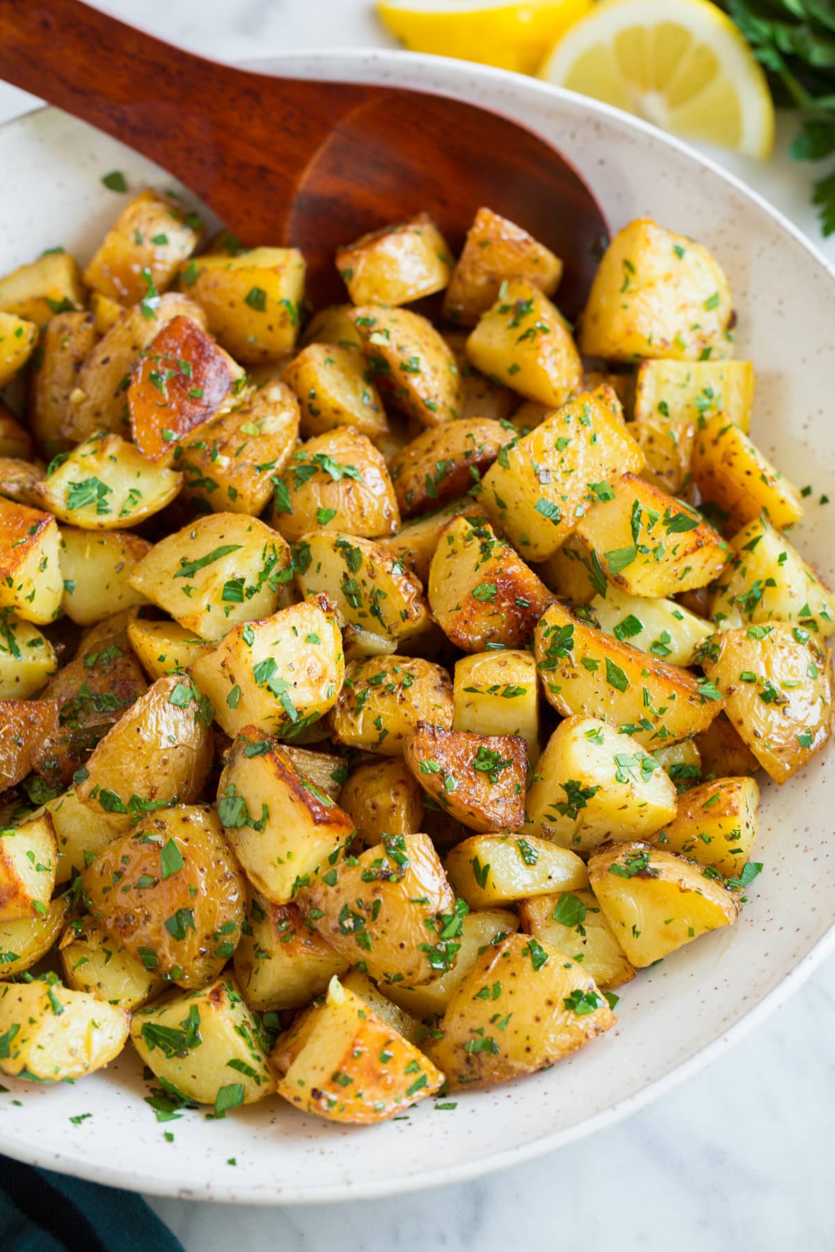 Lemon Roasted Potatoes Bowl of roasted potatoes with lemon and parsley, wooden spoon is resting in potatoes.