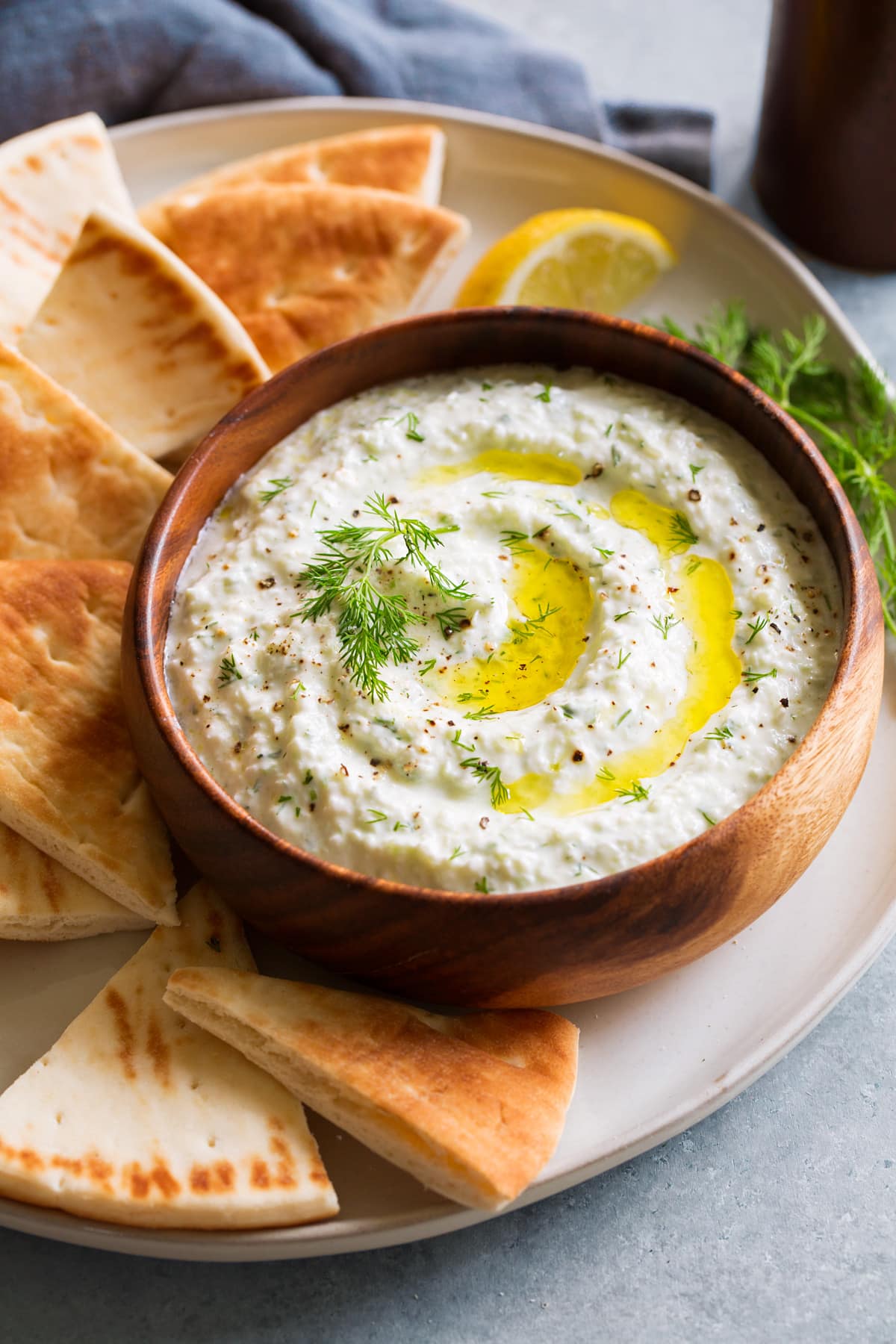 Homemade Tzatziki Sauce Bowl of homemade tzatziki sauce in wooden bowl on a platter with pita bread to the side.