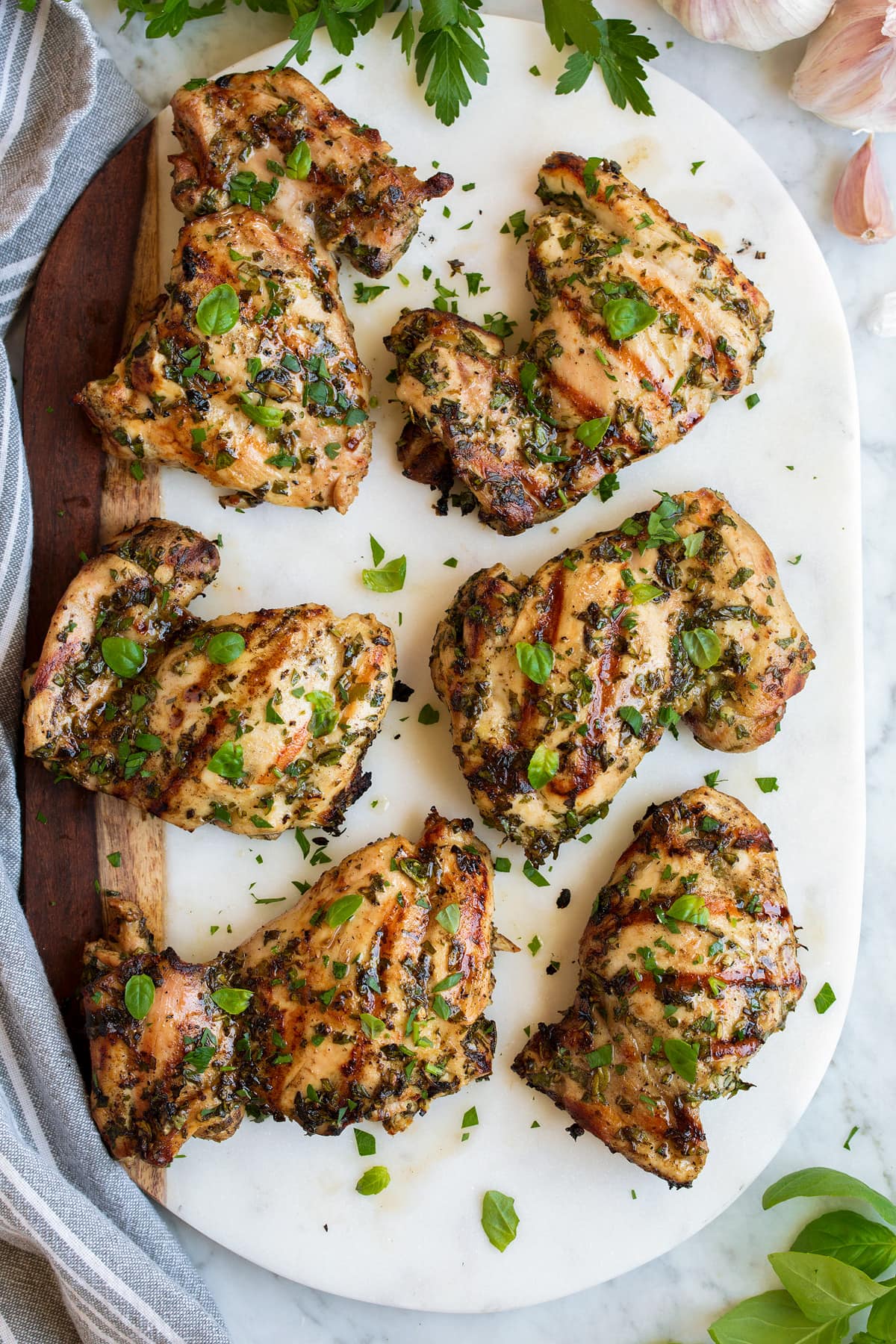 Garlic Herb Grilled Chicken Six pieces of Garlic Herb Grilled Chicken shown overhead resting on a marble and wooden platter.