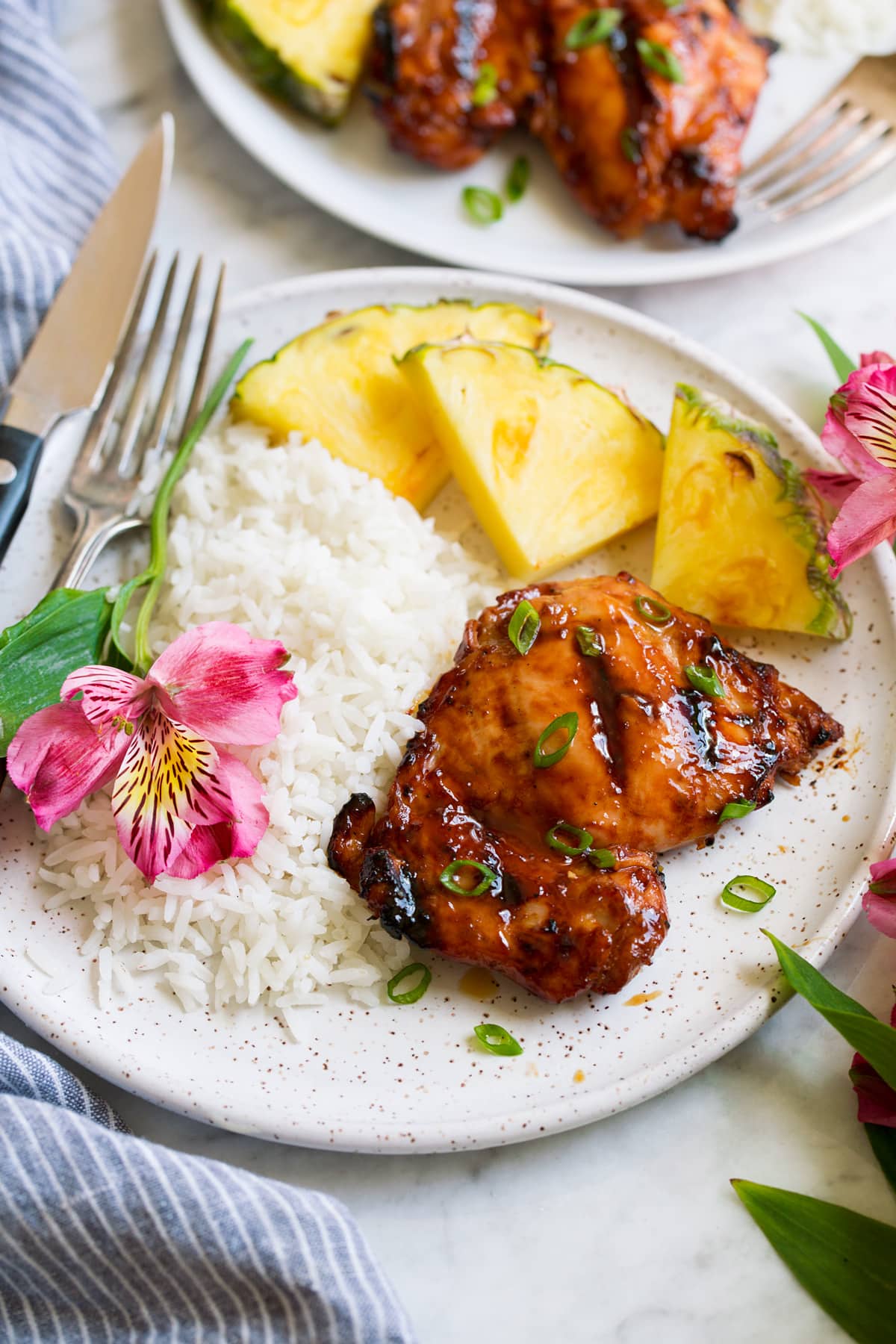 Huli Huli Chicken Plate with 1 huli huli chicken piece, pineapple, rice and a fresh flower. Shown from the side.