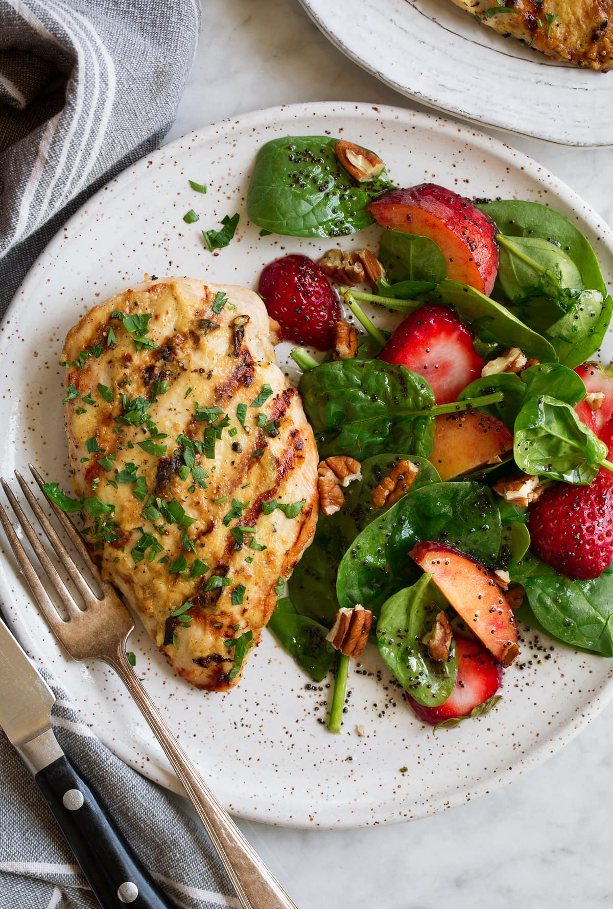 Grilled Dijon Chicken Dijon chicken shown on a serving plate with a side of spinach strawberry salad and poppy seed dressing.
