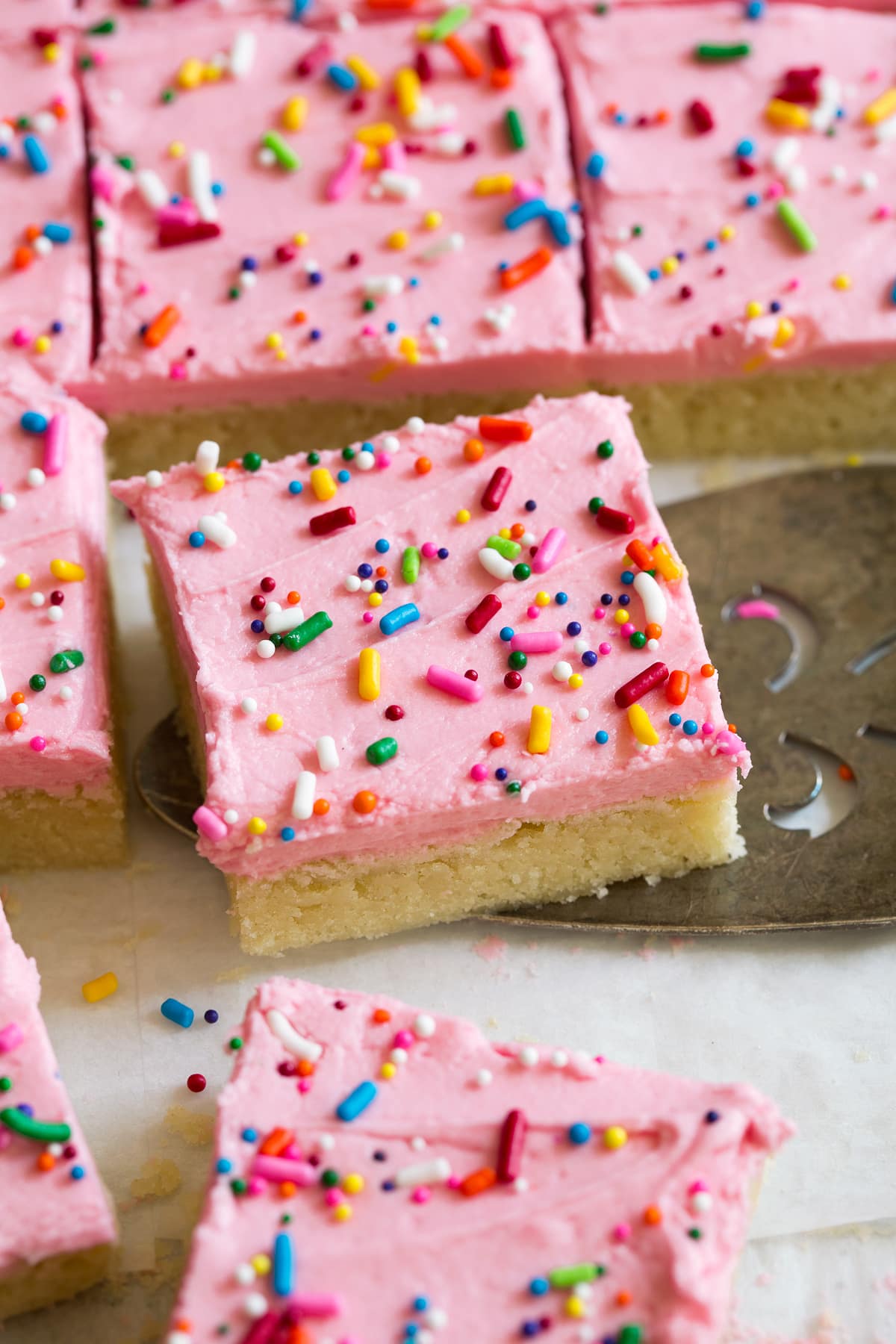Sugar Cookie Bars Close up image of sugar cookie bar decorated with pink frosting and sprinkles. It is being scooped up with a serving spatula.