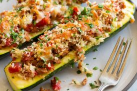 Two stuffed zucchini boats on a white dinner plate with a fork to the side.
