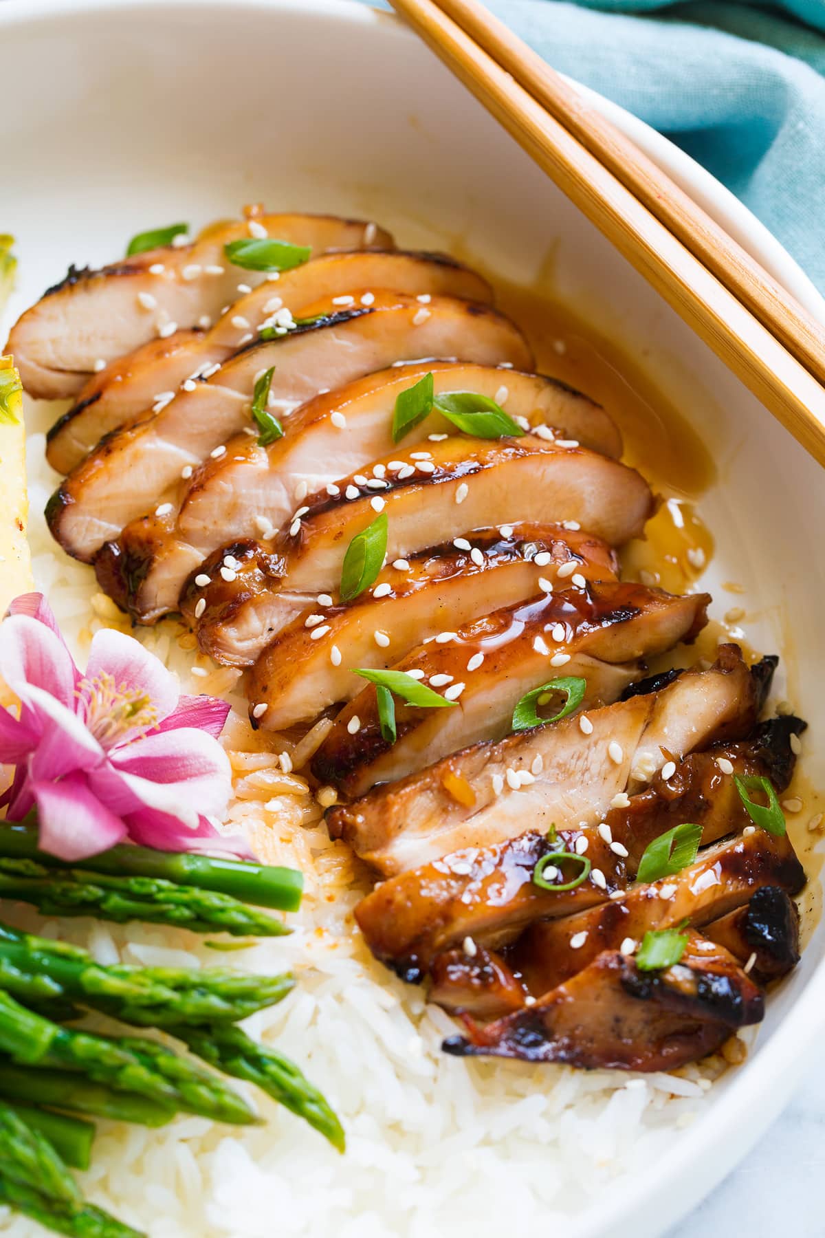 Marinated Grilled Teriyaki Chicken Sliced chicken thigh shown after cooking, covered in teriyaki sauce, sesame seeds and green onions.