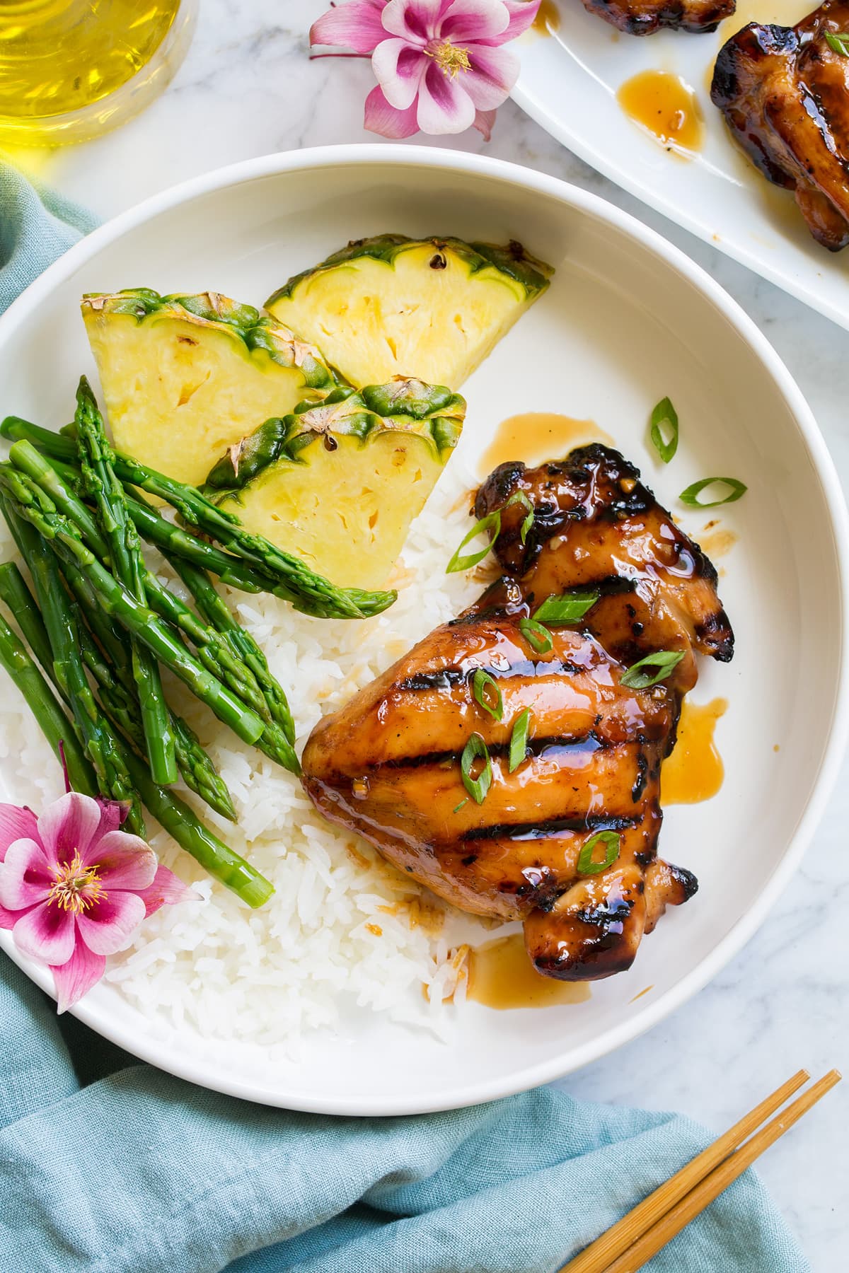 Marinated Grilled Teriyaki Chicken Piece of marinated and grilled teriyaki chicken shown served with rice, asparagus and fresh pineapple.