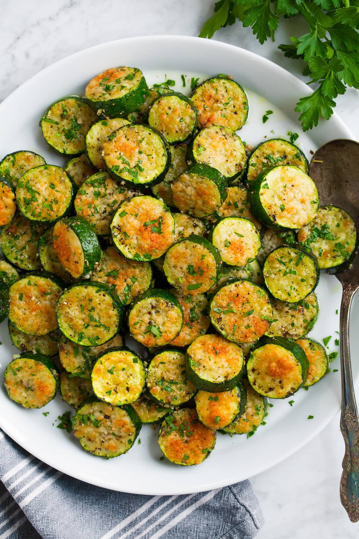 Baked Zucchini Baked zucchini coins covered with parmesan shown overhead on a white plate.