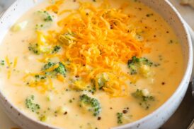 Single serving of broccoli cheese soup in a white bowl with crackers to the side.