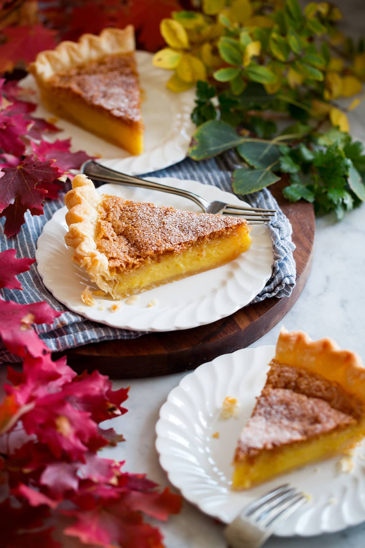 Chess Pie Three slices of chess pie shown on white dessert plates with vibrantly colored fall leaves surrounding.