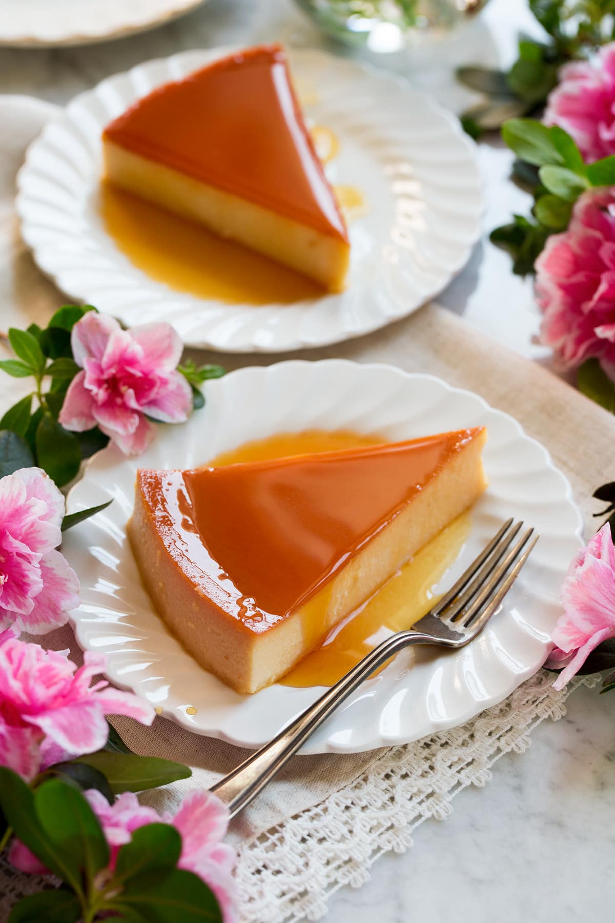 Flan Recipe Image of two slices of flan on white scalloped plates with flowers around the sides.