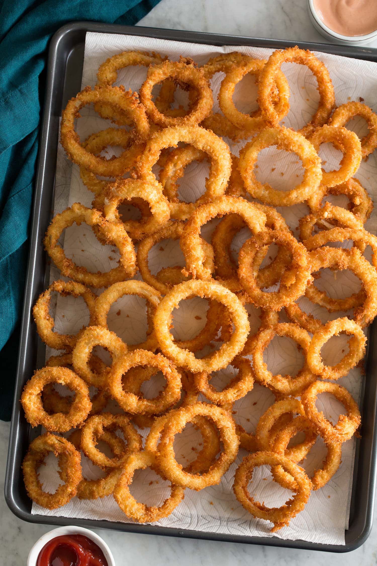 Onion Rings Fried onion rings over paper towels on a baking sheet.