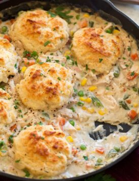 Image of Chicken Pot Pie with Biscuits shown in a cast iron skillet with a scoop removed from pot pie.