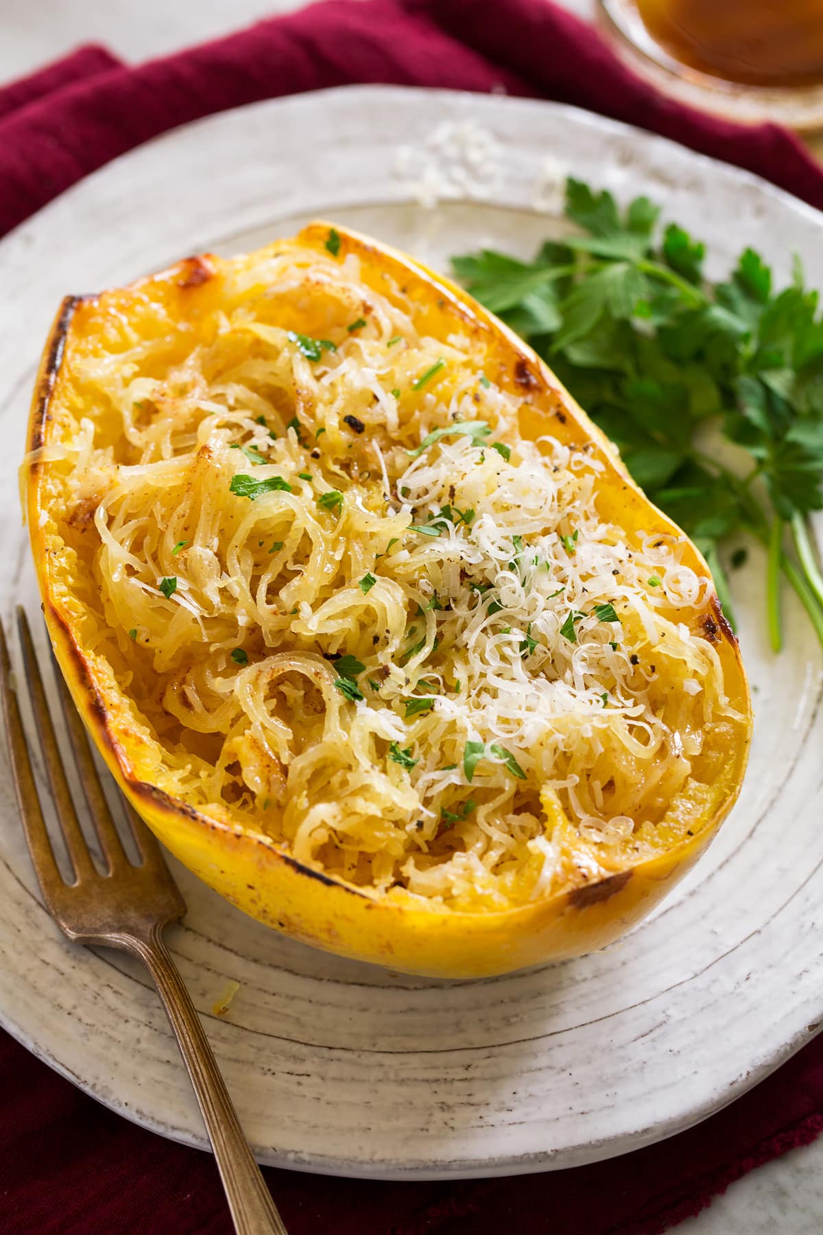 Roasted Spaghetti Squash with Browned Butter and Parmesan Roasted spaghetti squash half on a white serving plate. Squash it topped with browned butter, parmesan and parsley.