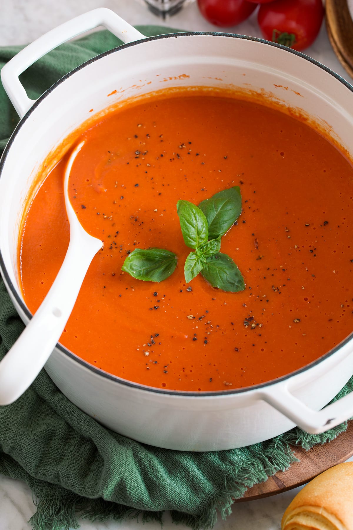 Homemade Tomato Soup Image of white pot filled with tomato soup that's garnished with basil and pepper.