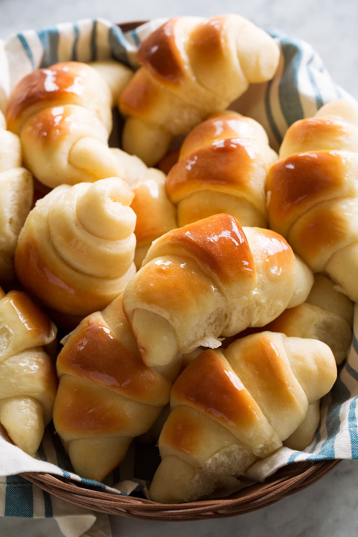 Homemade dinner rolls shown in a basket with a blue striped cloth.