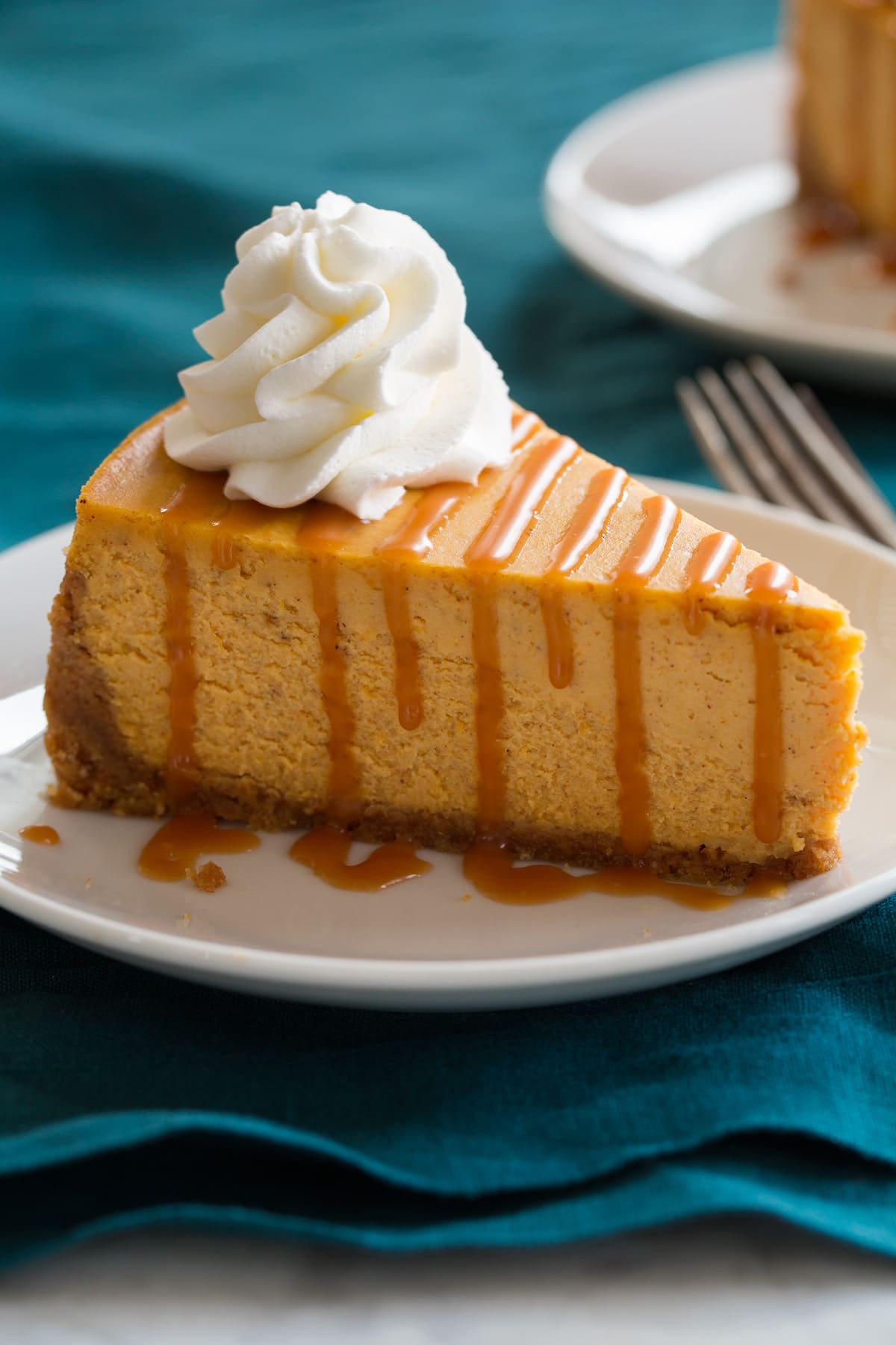 Close up image of slice of pumpkin cheesecake that is topped with caramel sauce and whipped cream.