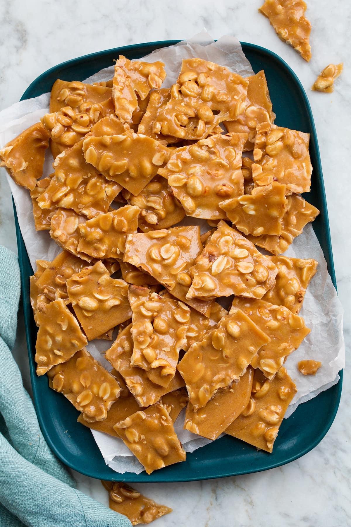 Peanut Brittle Peanut Brittle shown from above on a rectangular blue platter covered with parchment paper.
