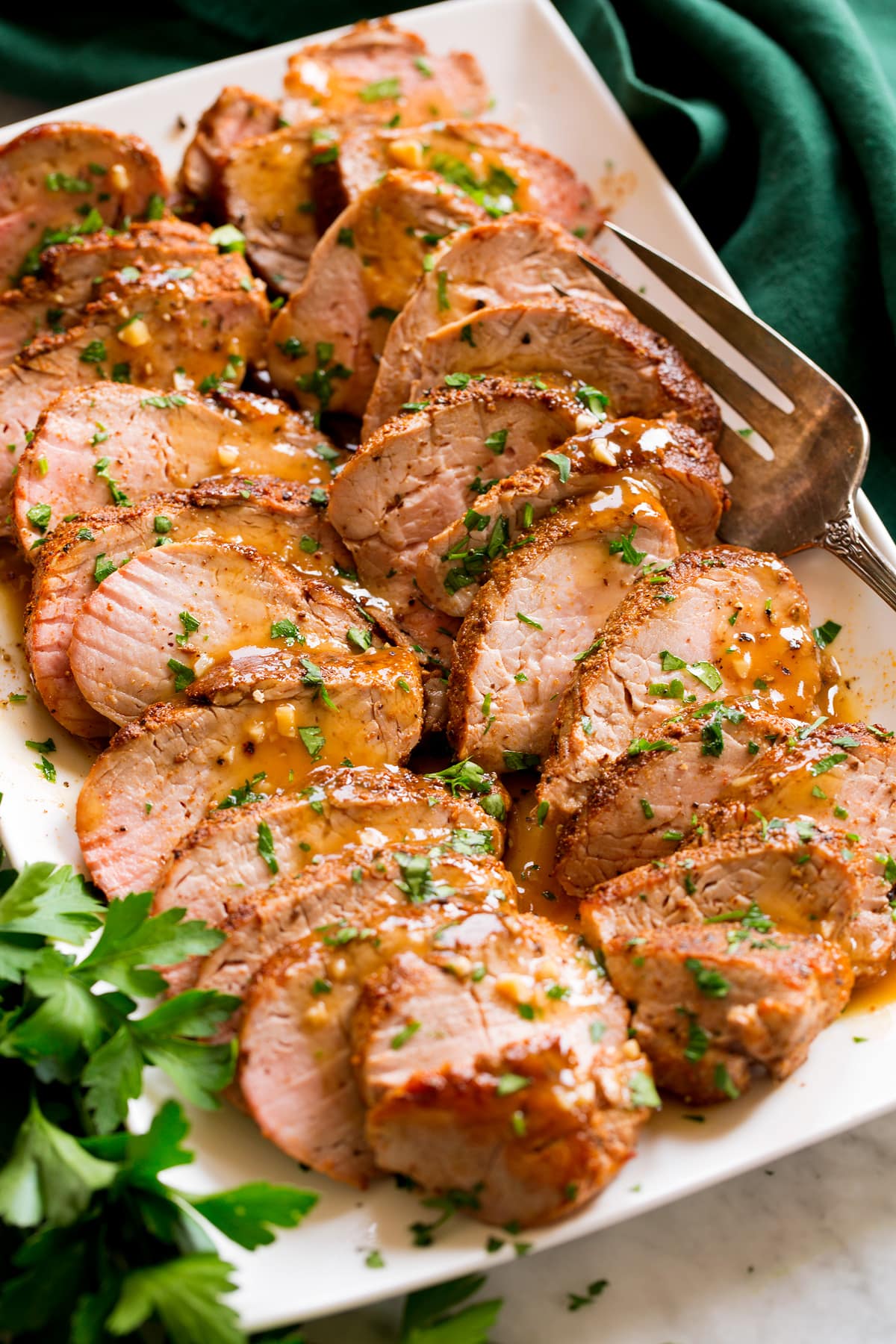 Baked Pork Tenderloin Baked Pork Tenderloin sliced into strips resting shown on a platter. Pork is rubbed with spices, topped with a pan sauce and parsley.