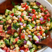Chickpea Salad shown in a serving bowl with wooden serving spoons.