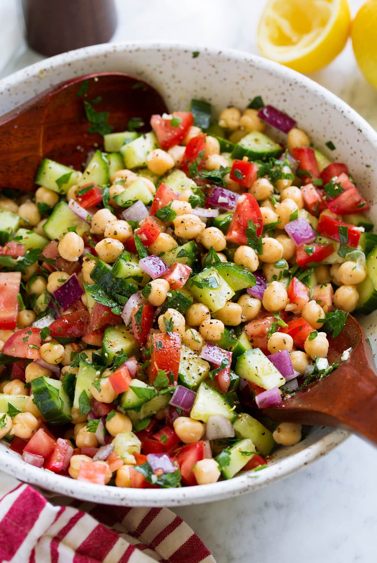 Chickpea Salad shown in a serving bowl with wooden serving spoons.