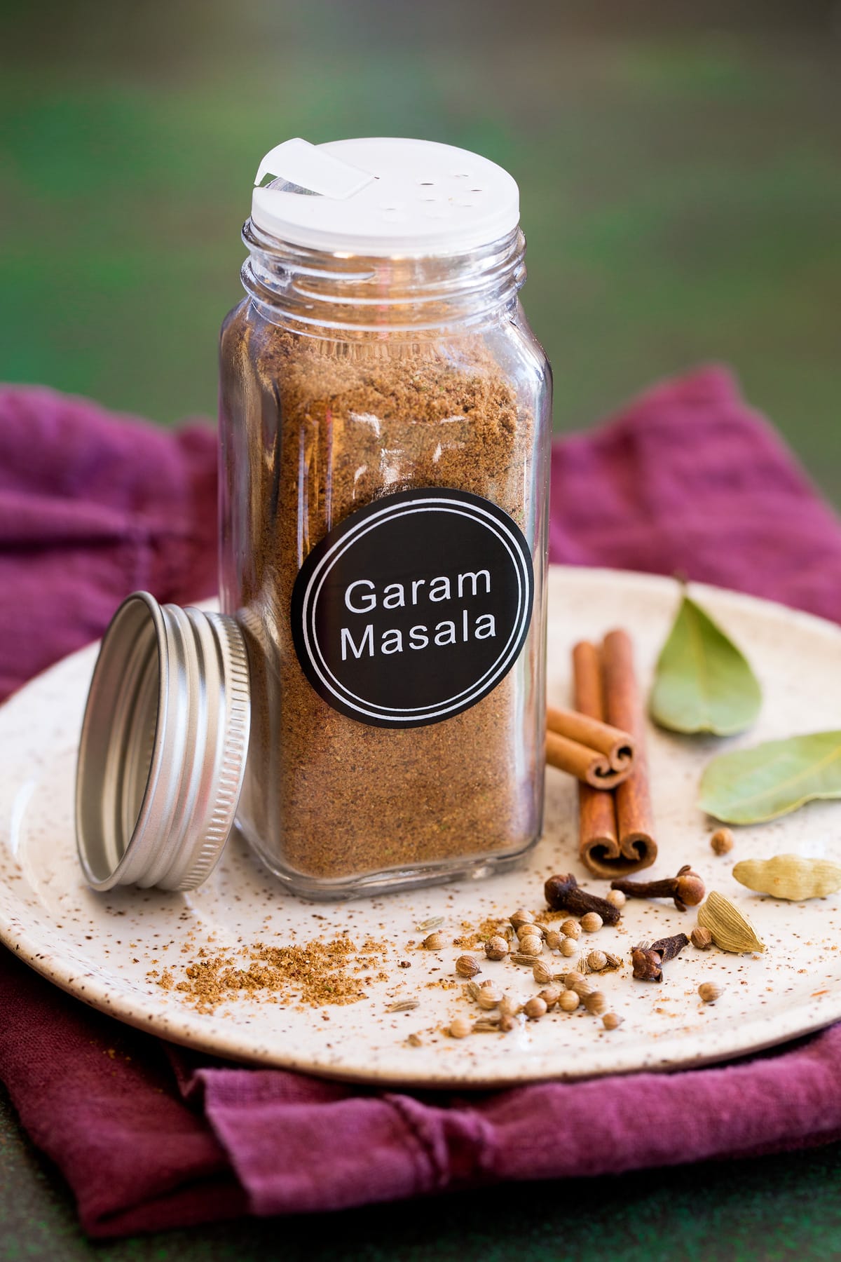 Garam Masala Garam masala spice blend in a glass jar set over a plate with whole spices next to it.