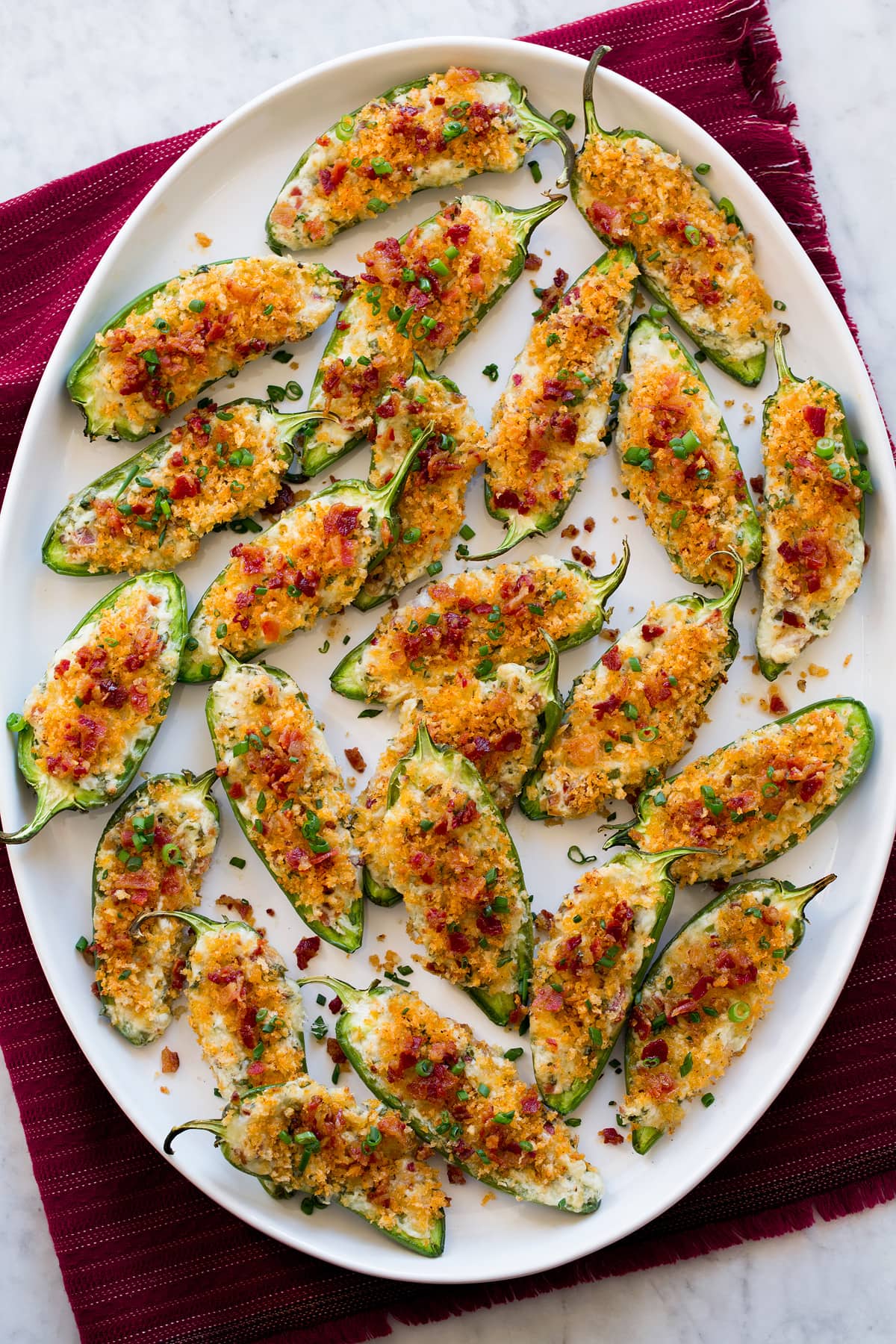 Jalapeno Poppers Overhead photo of jalapeno poppers on oval white platter over red cloth.