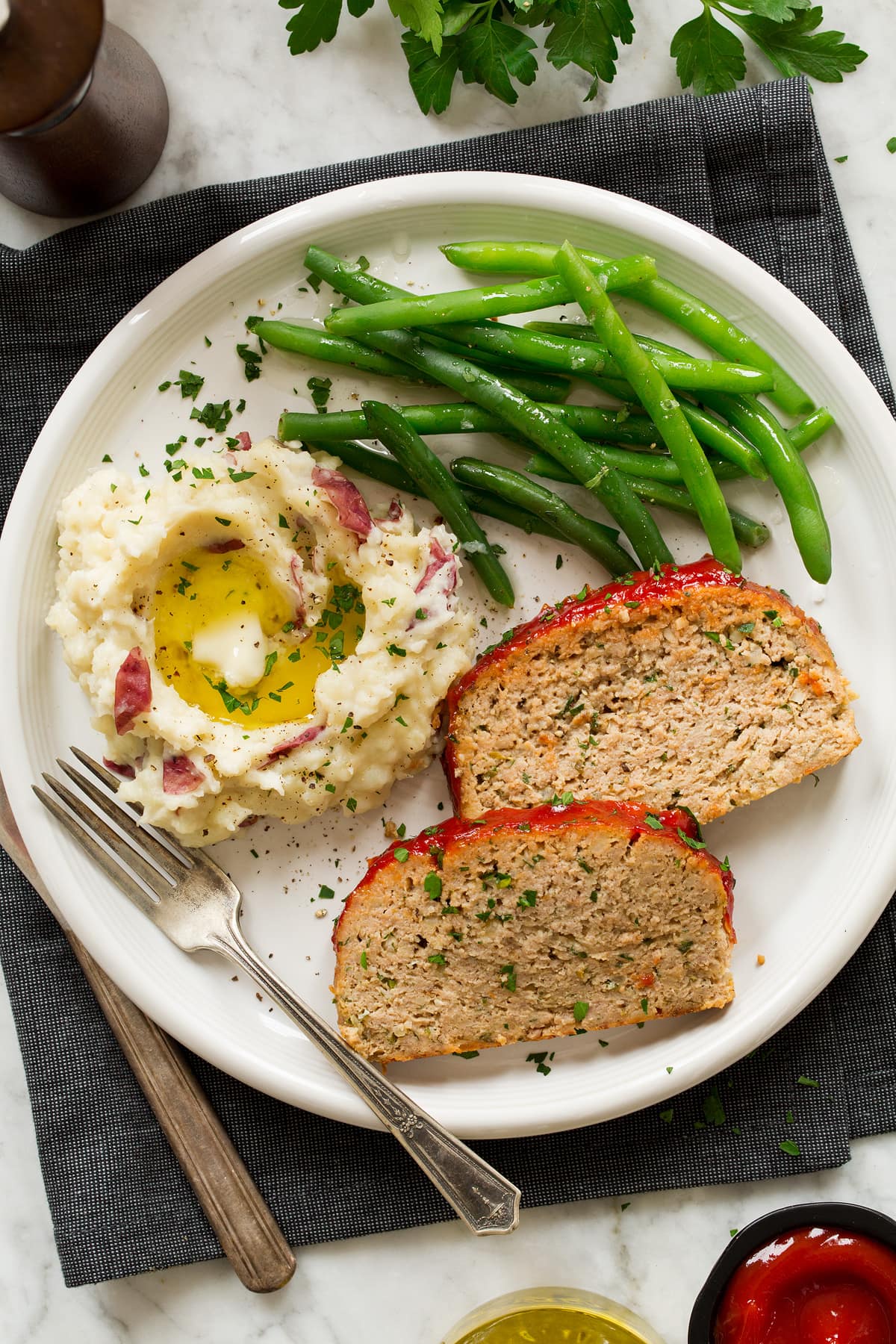 Turkey Meatloaf Two slices of turkey meatloaf shown on a serving plate with serving suggestions of mashed potatoes and green beans.