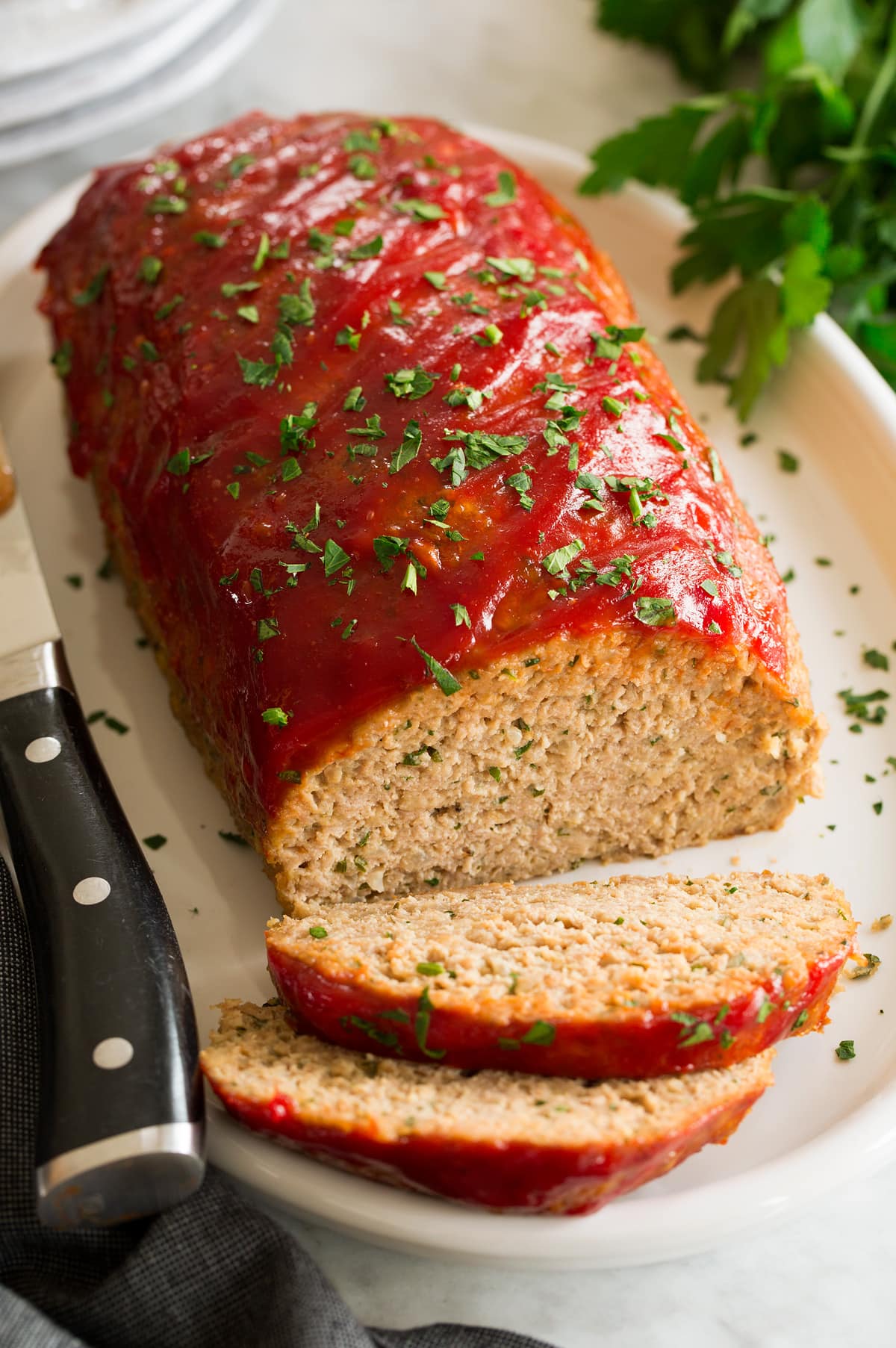 Turkey Meatloaf Photo of turkey meatloaf on a white oval serving platter. Parsley is sprinkled over and whole parsley is to the side. A large knife is shown to the side.