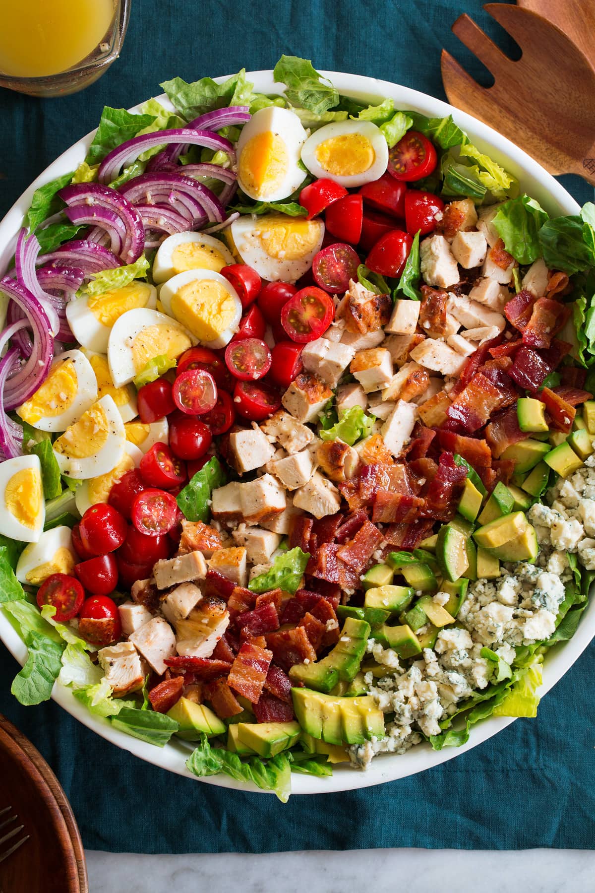 Cobb Salad Overhead photo of cobb salad with blue cheese, avocado, bacon, chicken, tomatoes, hard boiled eggs, red onion and romaine lettuce in a large white bowl.