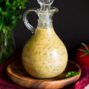 Photo: Italian Dressing in a glass bottle set over a wooden plate and a red cloth.