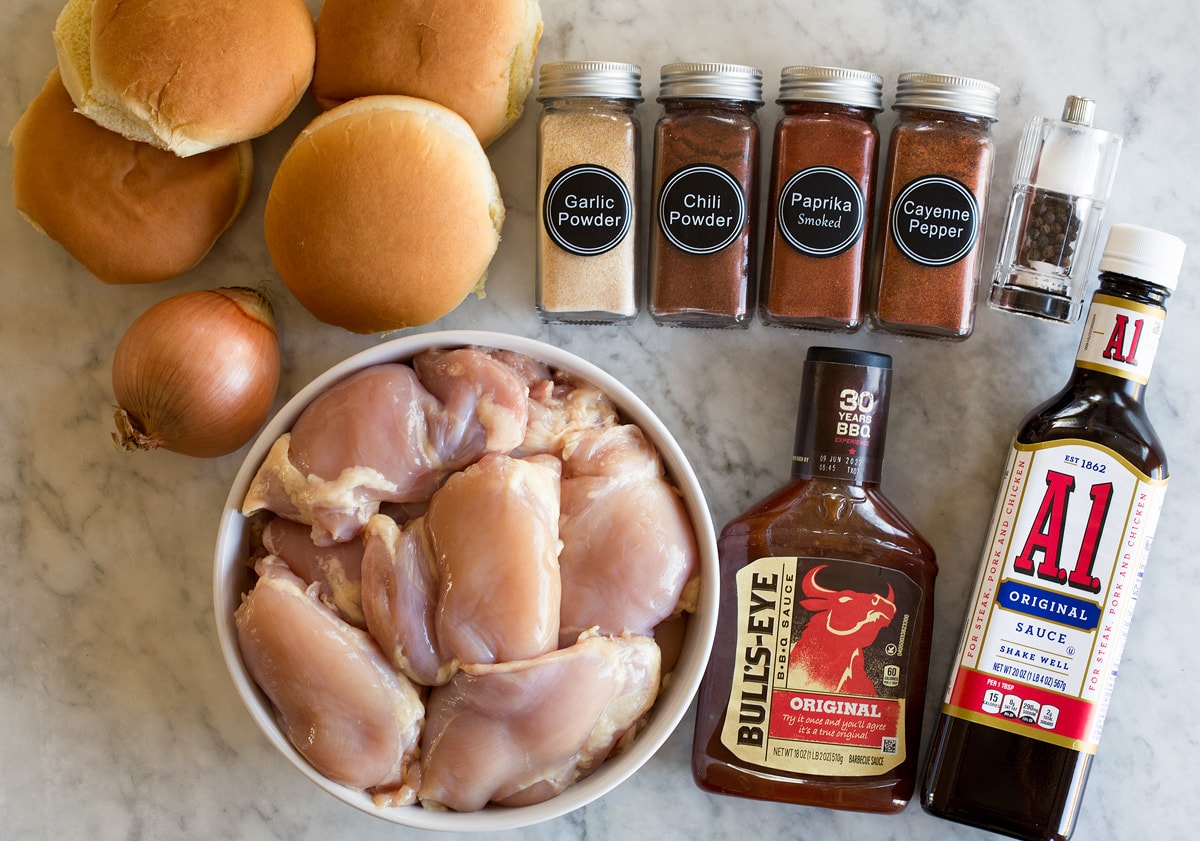 Crockpot BBQ Chicken Photo: Ingredients used to make slow cooker barbecue chicken. Includes chicken thighs, bbq sauce, steak sauce, chili powder, smoked paprika, garlic powder, cayenne pepper, salt, pepper, buns, and yellow onion.