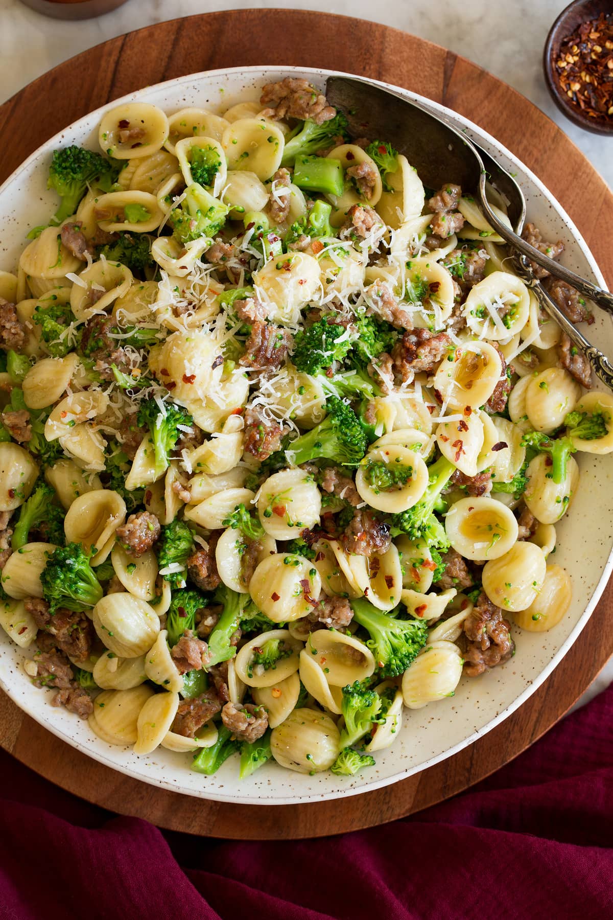 Orecchiette with Sausage and Broccoli Photo: Orecchiette pasta with sausage and broccoli in a white serving bowl set over a wooden platter on a marble surface. It is shown from above.