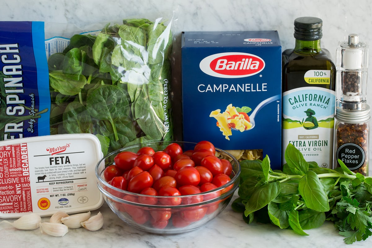 Baked Feta Pasta Photo: Ingredients shown that are needed for baked feta pasta. Includes pasta, feta, spinach, basil, parsley, tomatoes, garlic, olive oil, crushed red pepper flakes, salt and pepper.