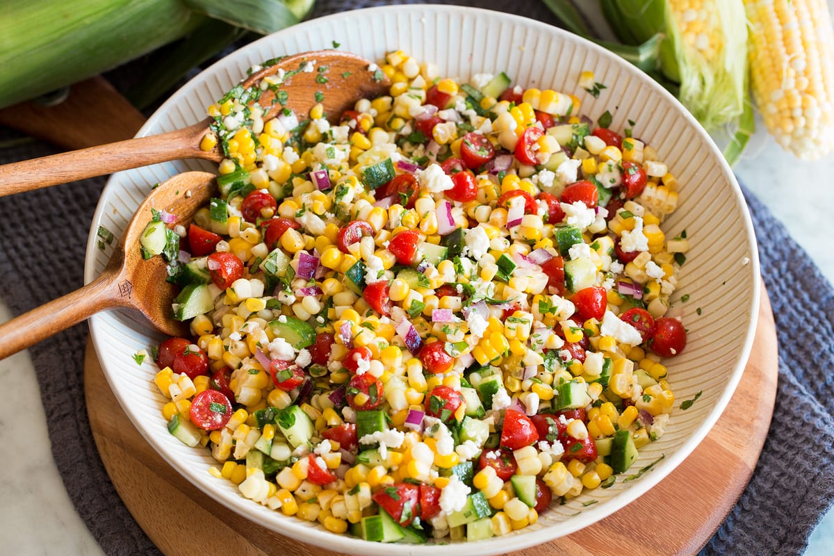 Corn Salad Photo: Completed corn salad after tossing all ingredients and dressing together shown in a white ribbed bowl over a wooden platter.